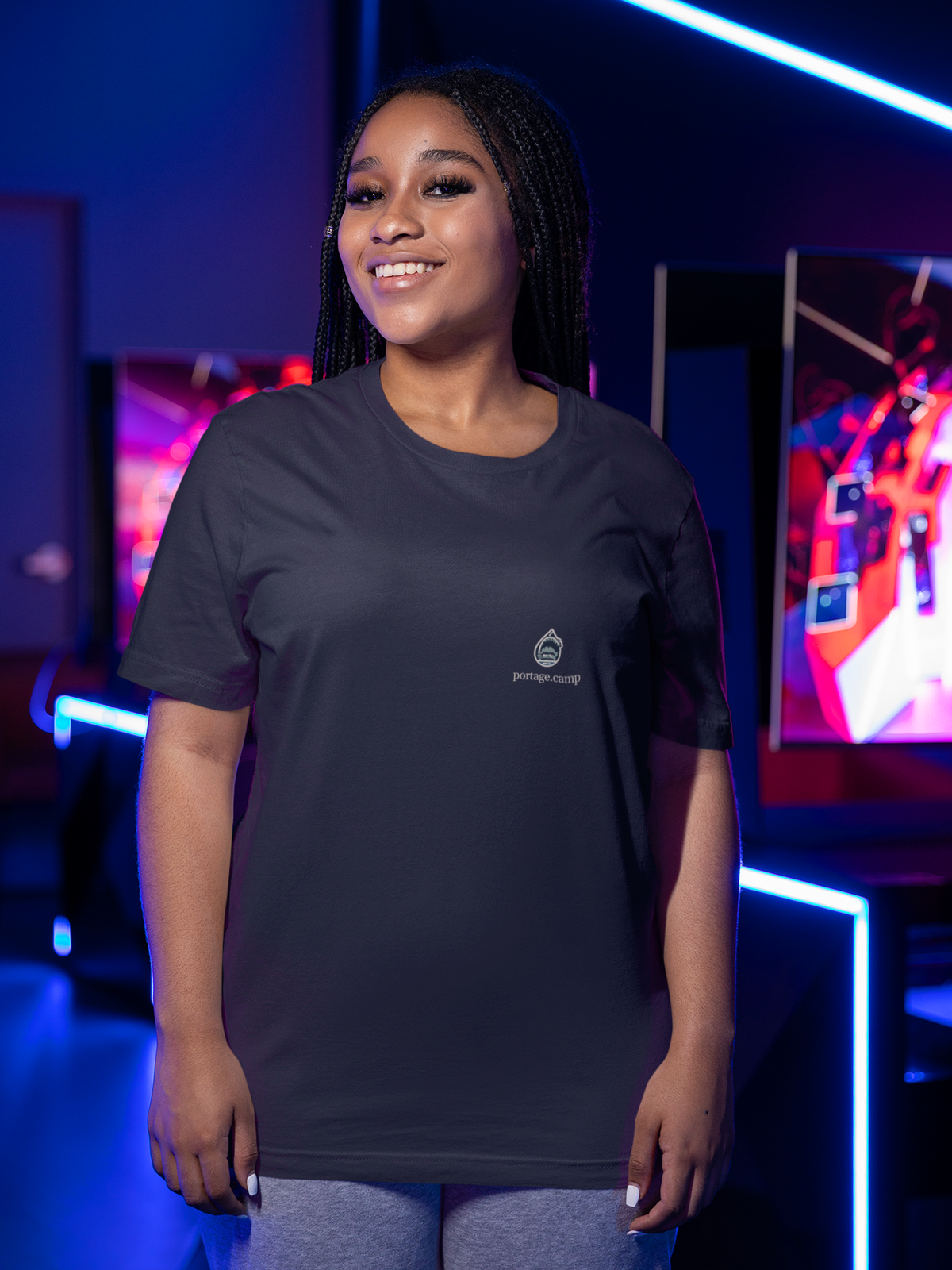 Rain Check Garment-Dyed Tee in Black, worn by a woman under neon lights in a gaming arcade, with the Rain Check logo and portage.camp on the chest. Digital product mockup.