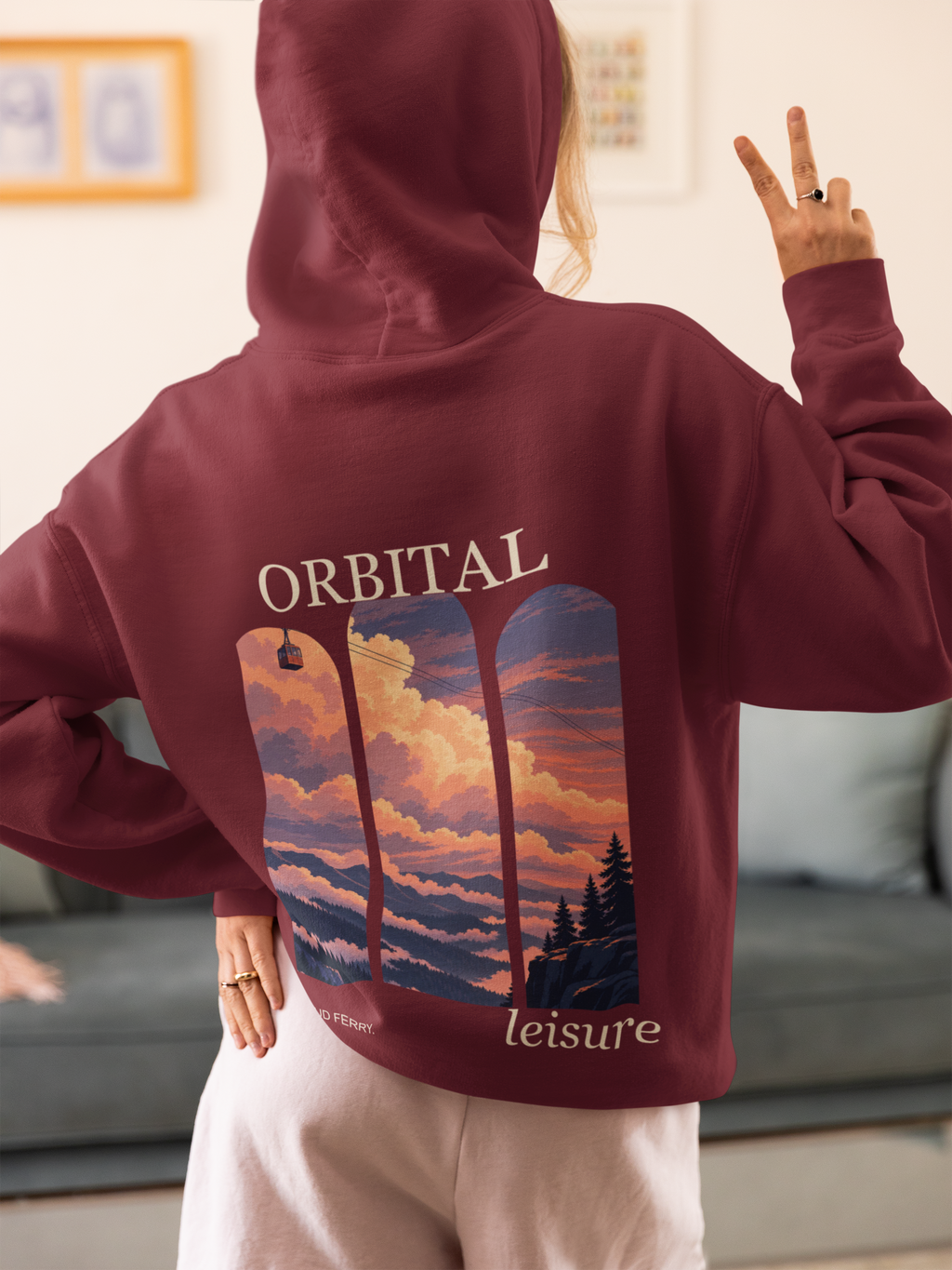 Cloud Ferry Midweight Hoodie in Maroon, worn by a woman seen from behind at home, making a peace sign, showing the large print on the back. Digital product mockup.