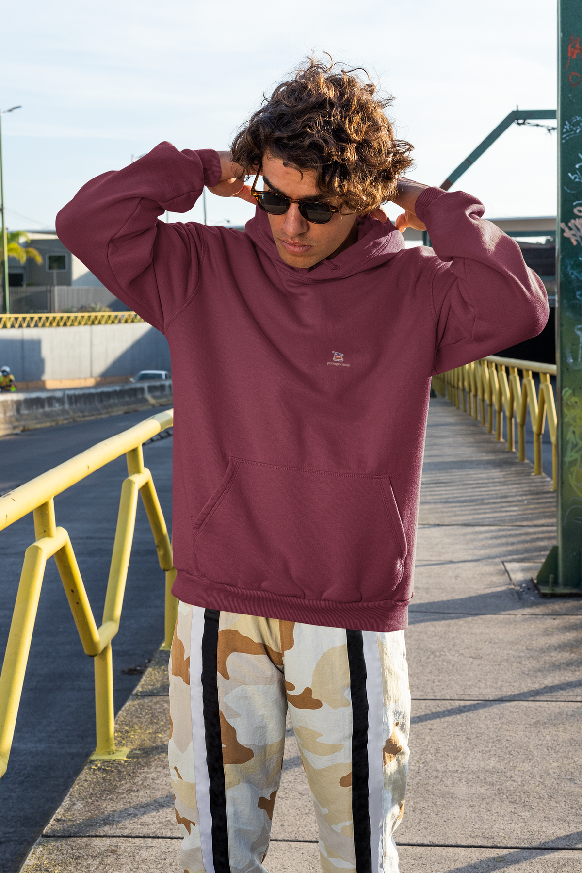 Cloud Ferry Midweight Hoodie in Maroon, worn by a man on a city street, with the Cloud Ferry logo and portage.camp on the chest. Digital product mockup.