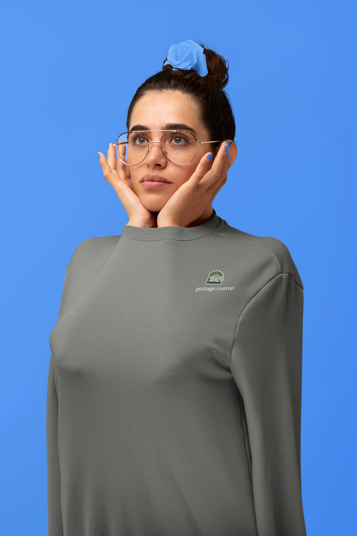 Rain Check Garment-Dyed Crewneck in Pepper, worn by a woman in a studio, arms tucked inside the sleeves, with the Rain Check logo and portage.camp on the chest. Digital product mockup.