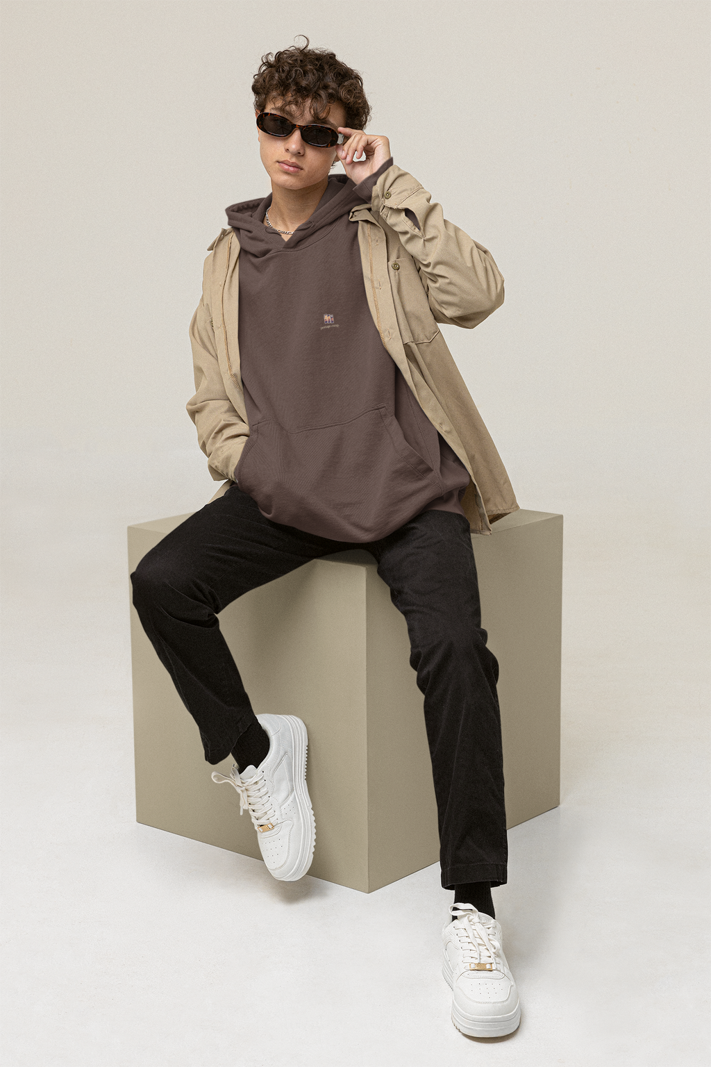 Stay for the Sky Heavyweight Hoodie in Brown, worn by a man seated on a block in a studio, with the Stay for the Sky logo and portage.camp on the left chest. Digital product mockup.