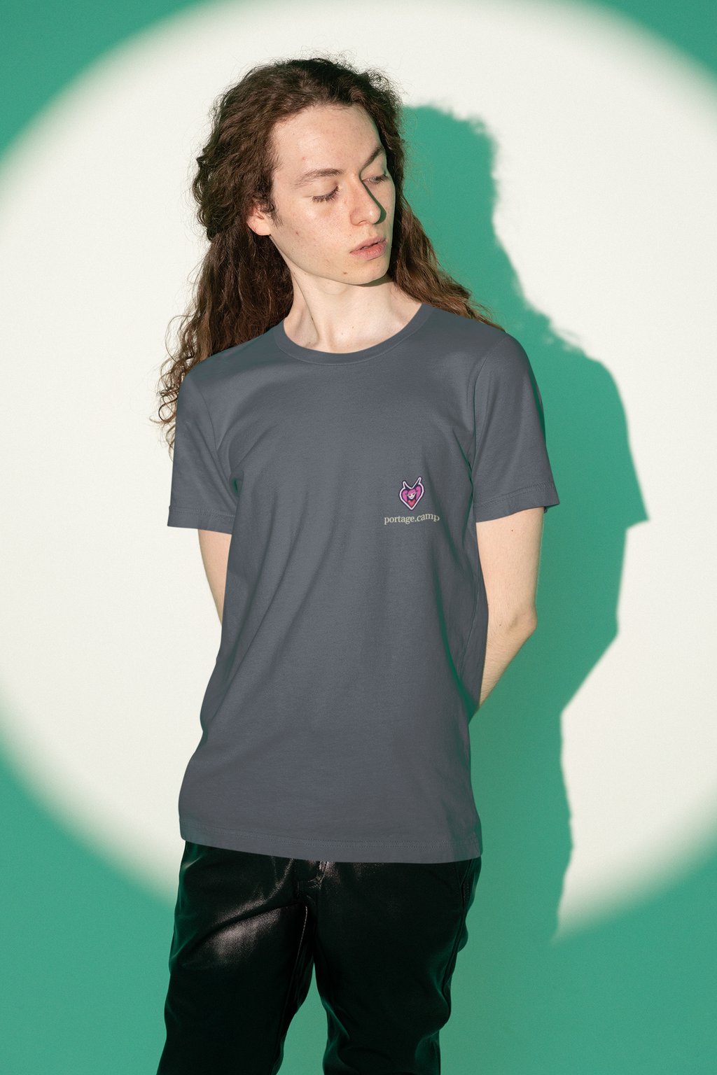 Heart Thief Garment-Dyed Tee in Navy, worn by a man against green studio light, with the Heart Thief logo and portage.camp on the chest. Digital product mockup.