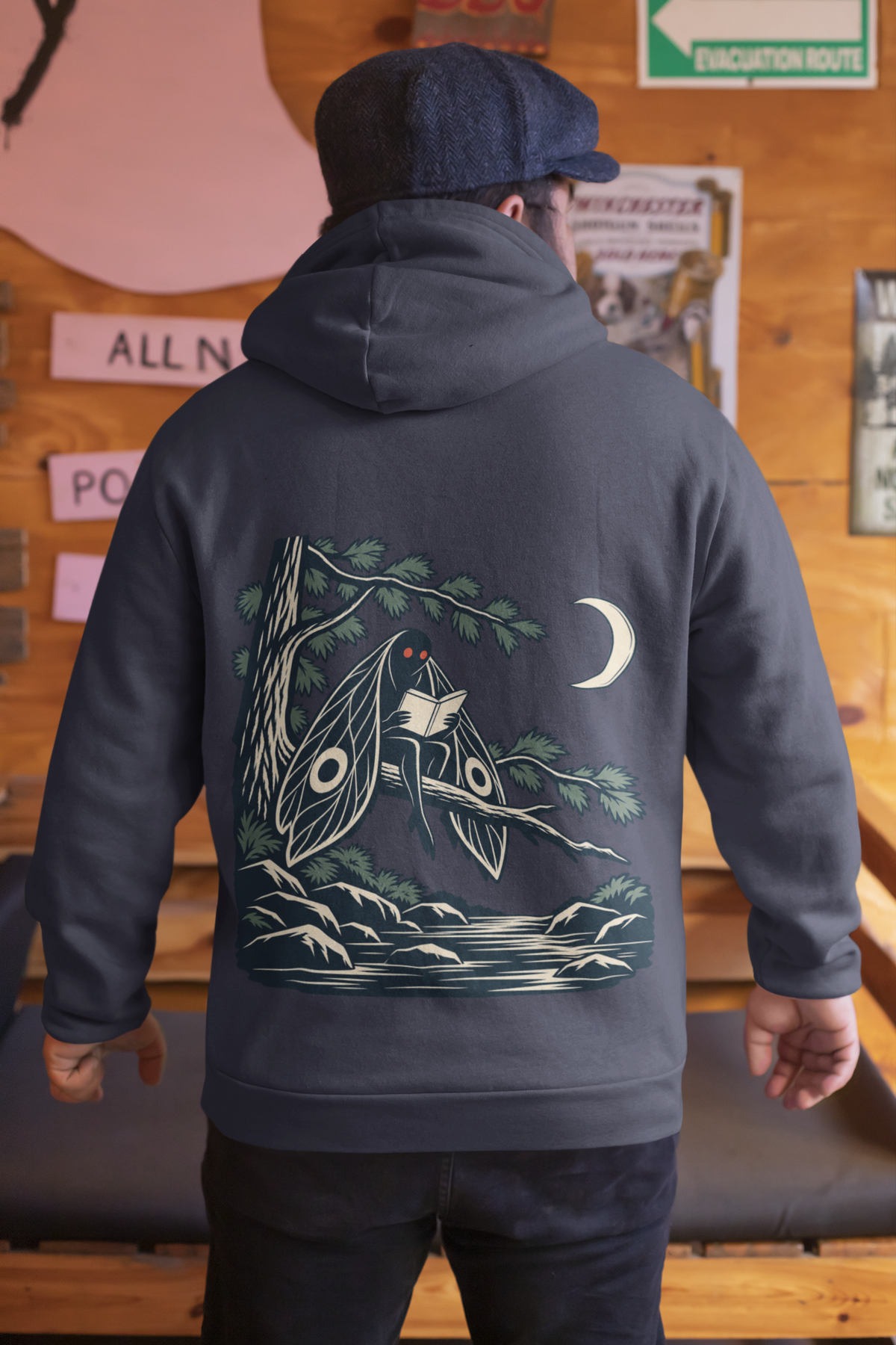 Night Library Midweight Hoodie in Classic Navy, worn by a man seen from behind in a wood-panelled bar, showing the large print on the back. Digital product mockup.