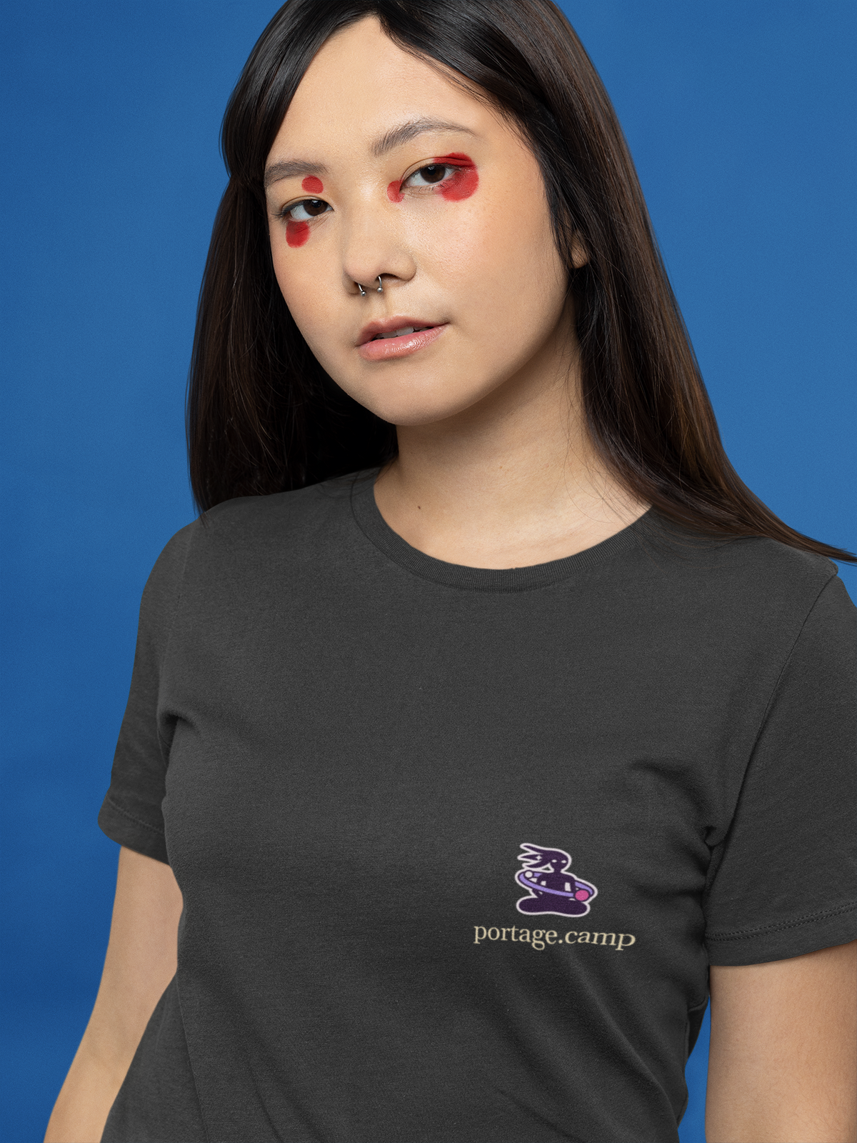 Orbit Keeper Women’s Relaxed Tee in Black, worn by a woman with graphic eyeliner, close up, with the Orbit Keeper logo and portage.camp on the chest. Digital product mockup.