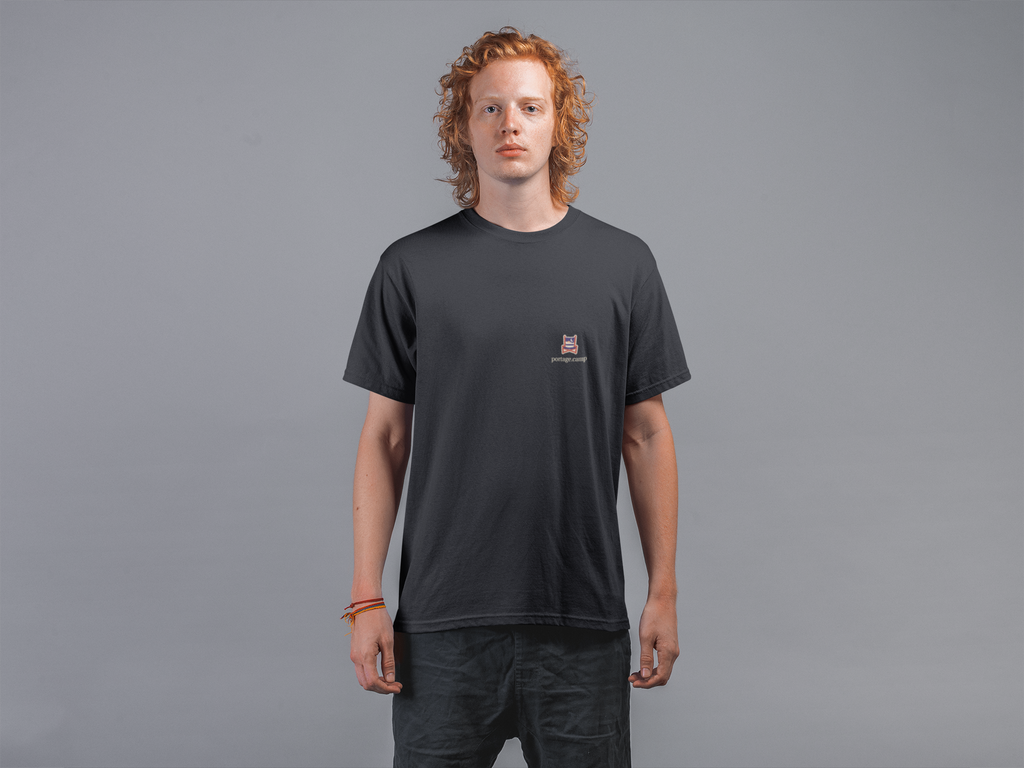 Edge of Evening Garment-Dyed Tee in Black, worn by a man against a plain grey wall, with the Edge of Evening logo and portage.camp on the chest. Digital product mockup.