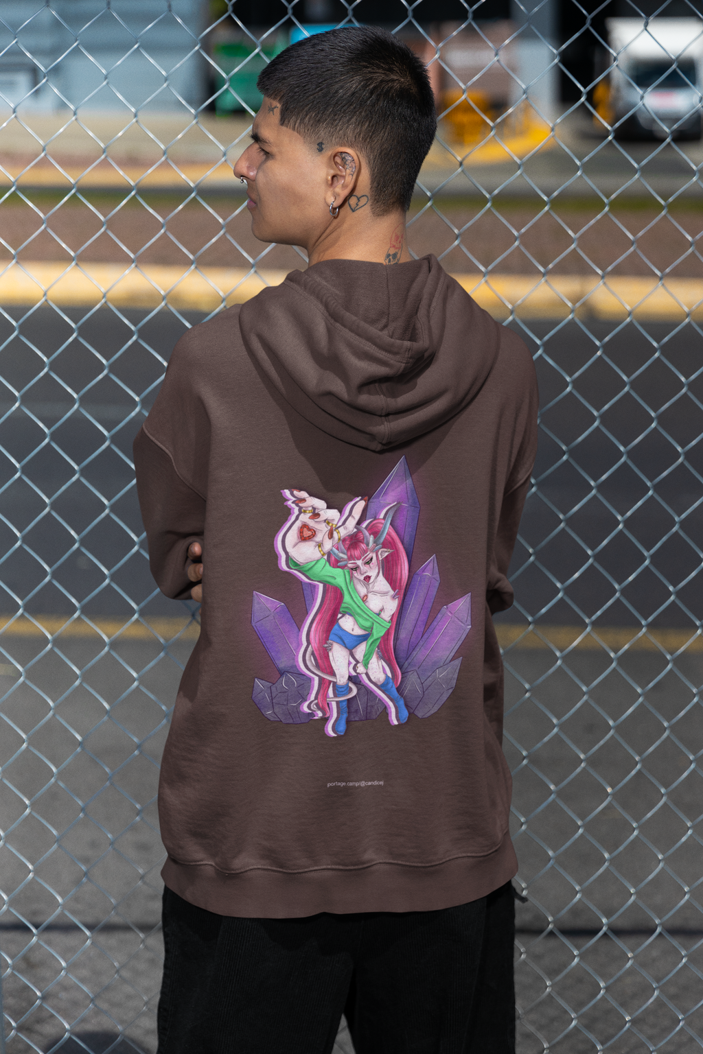 Amethyst After Hours Heavyweight Hoodie in Brown, worn by a man seen from behind by a chain-link fence, showing the large print on the back. Digital product mockup.