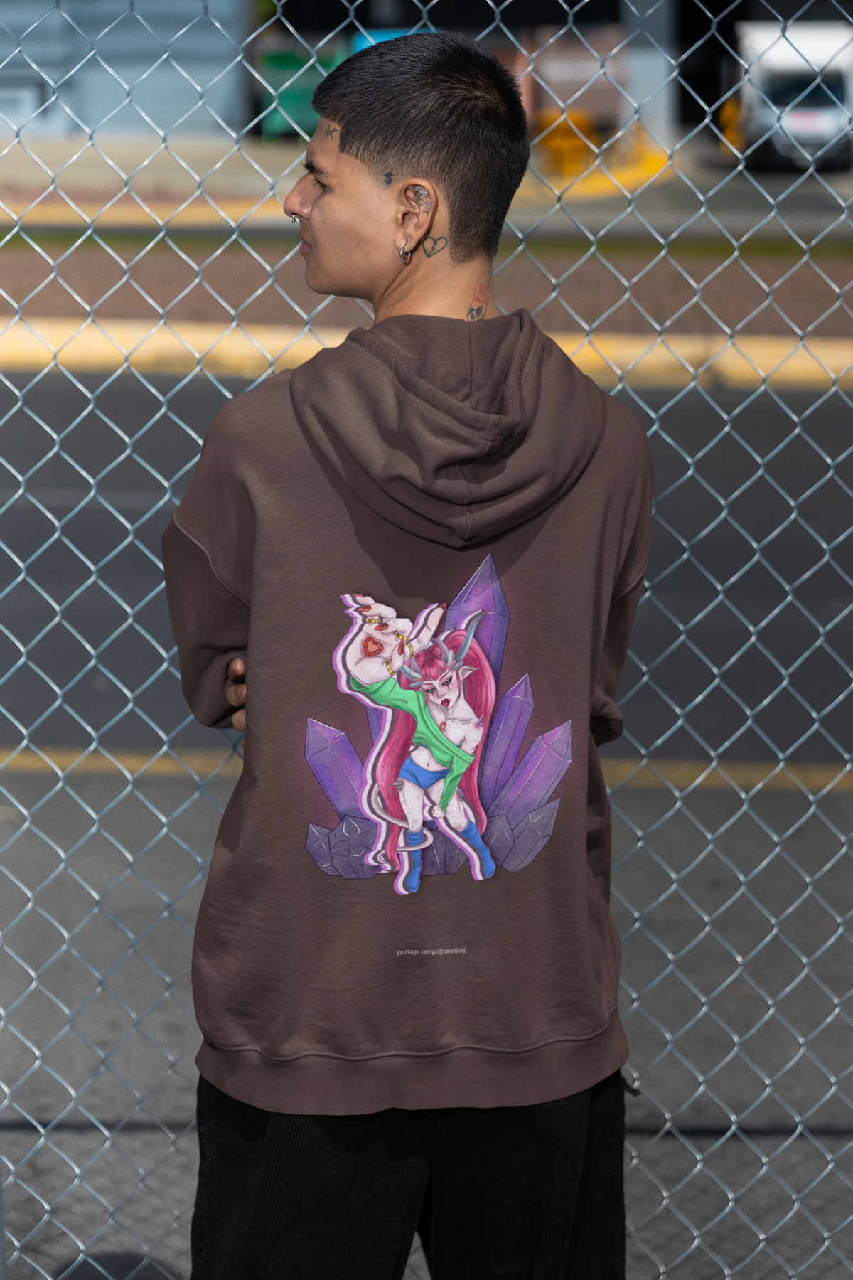 Amethyst After Hours Heavyweight Hoodie in Brown, worn by a man seen from behind by a chain-link fence, showing the large print on the back. Digital product mockup.