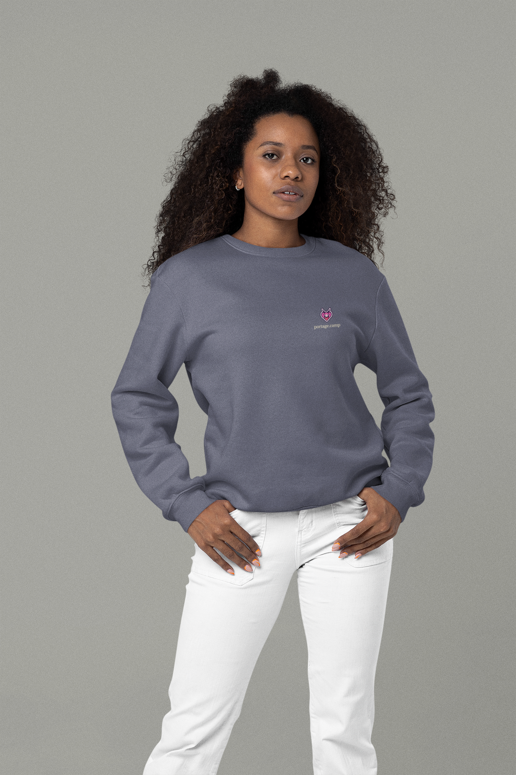 Heart Thief Garment-Dyed Crewneck in Denim, worn by a woman in a studio with her hands in her pockets, with the Heart Thief logo and portage.camp on the chest. Digital product mockup.
