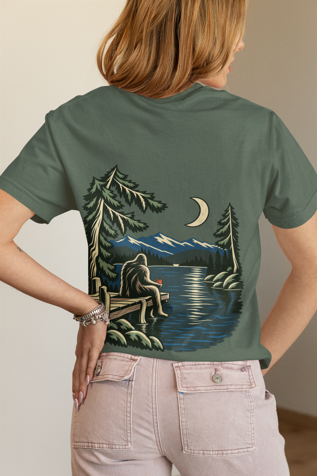 Quiet Hours Garment-Dyed Tee in Blue Spruce, worn by a woman seen from behind in a bedroom at home, showing the large print on the back. Digital product mockup.
