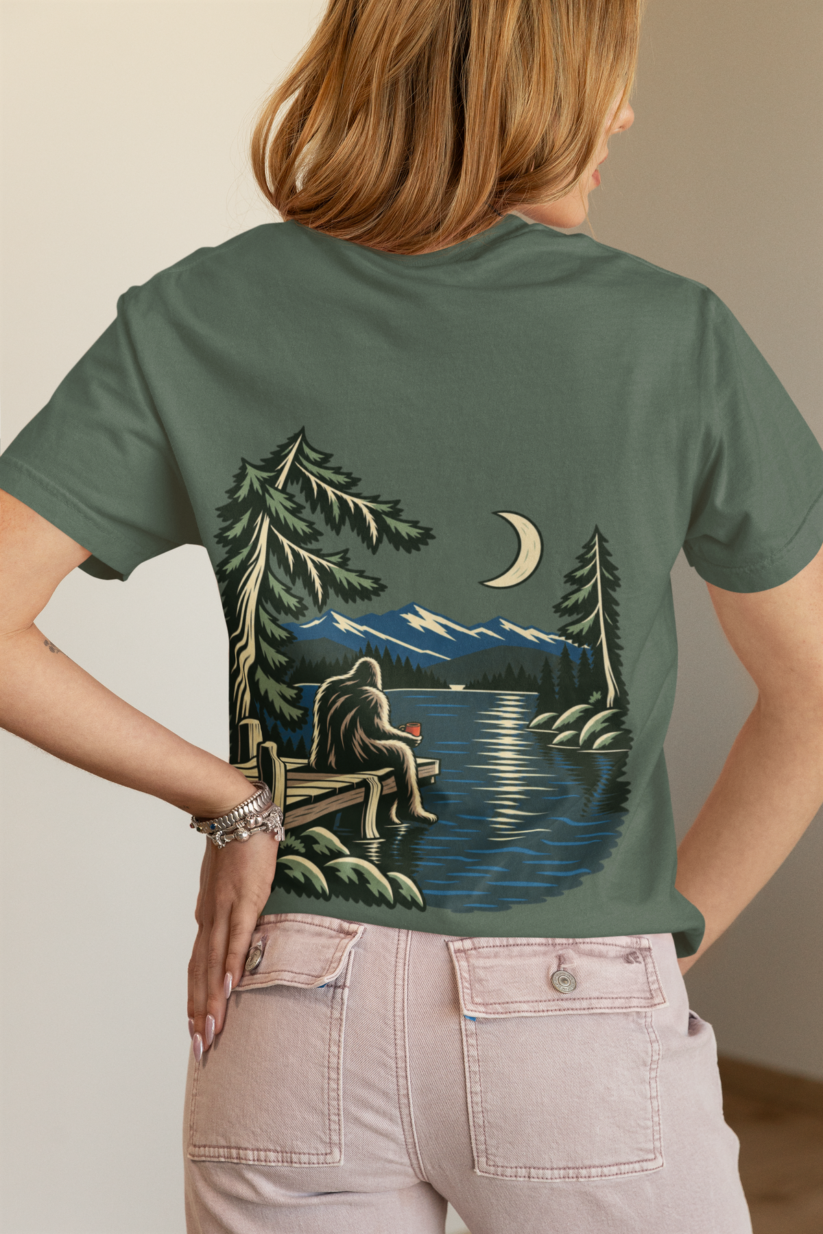 Quiet Hours Garment-Dyed Tee in Blue Spruce, worn by a woman seen from behind in a bedroom at home, showing the large print on the back. Digital product mockup.