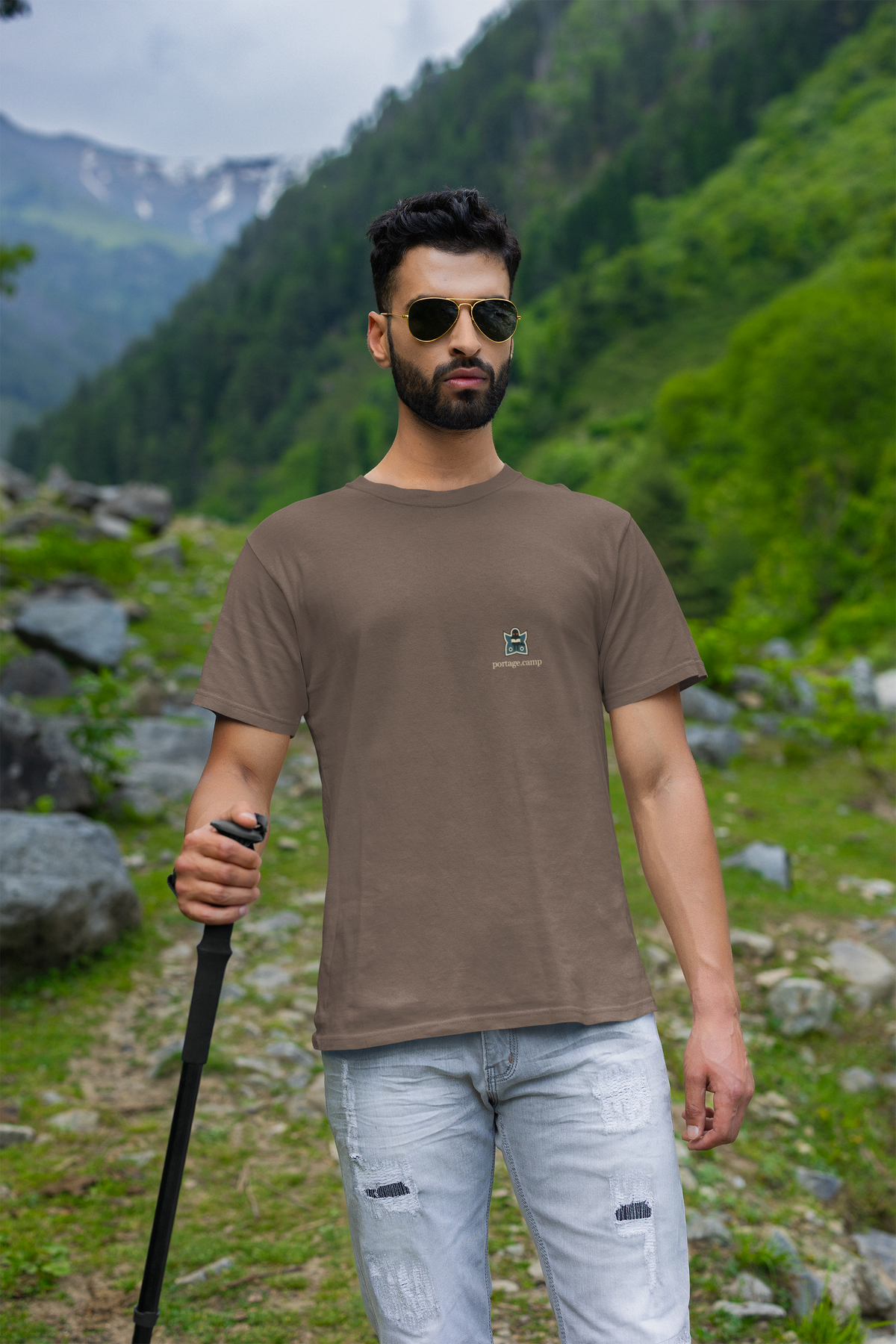 Night Library Garment-Dyed Tee in Espresso, worn by a man on a mountain trail, with the Night Library logo and portage.camp on the chest. Digital product mockup.