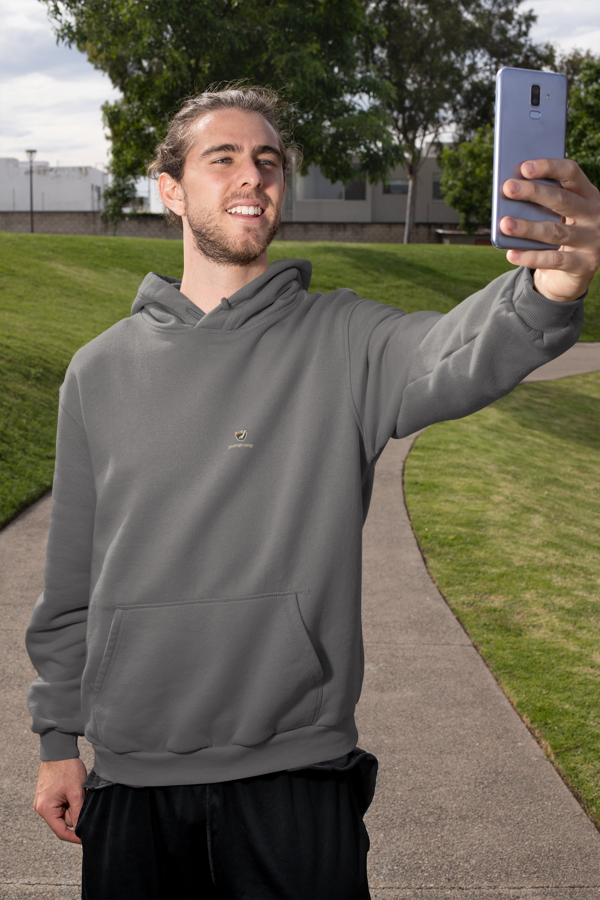 Seen Briefly Midweight Hoodie in Charcoal, worn by a man taking a selfie on a city street, with the Seen Briefly logo and portage.camp on the chest. Digital product mockup.