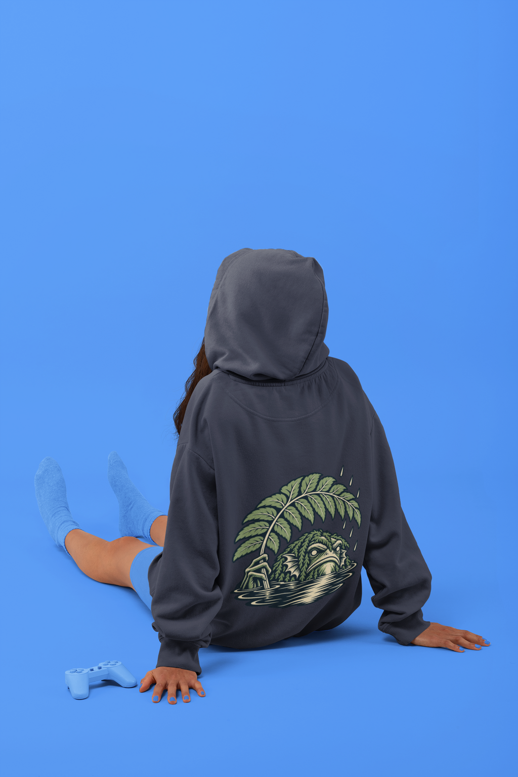 Rain Check Midweight Hoodie in Classic Navy, worn by a woman seen from behind seated on a studio floor, showing the large print on the back. Digital product mockup.