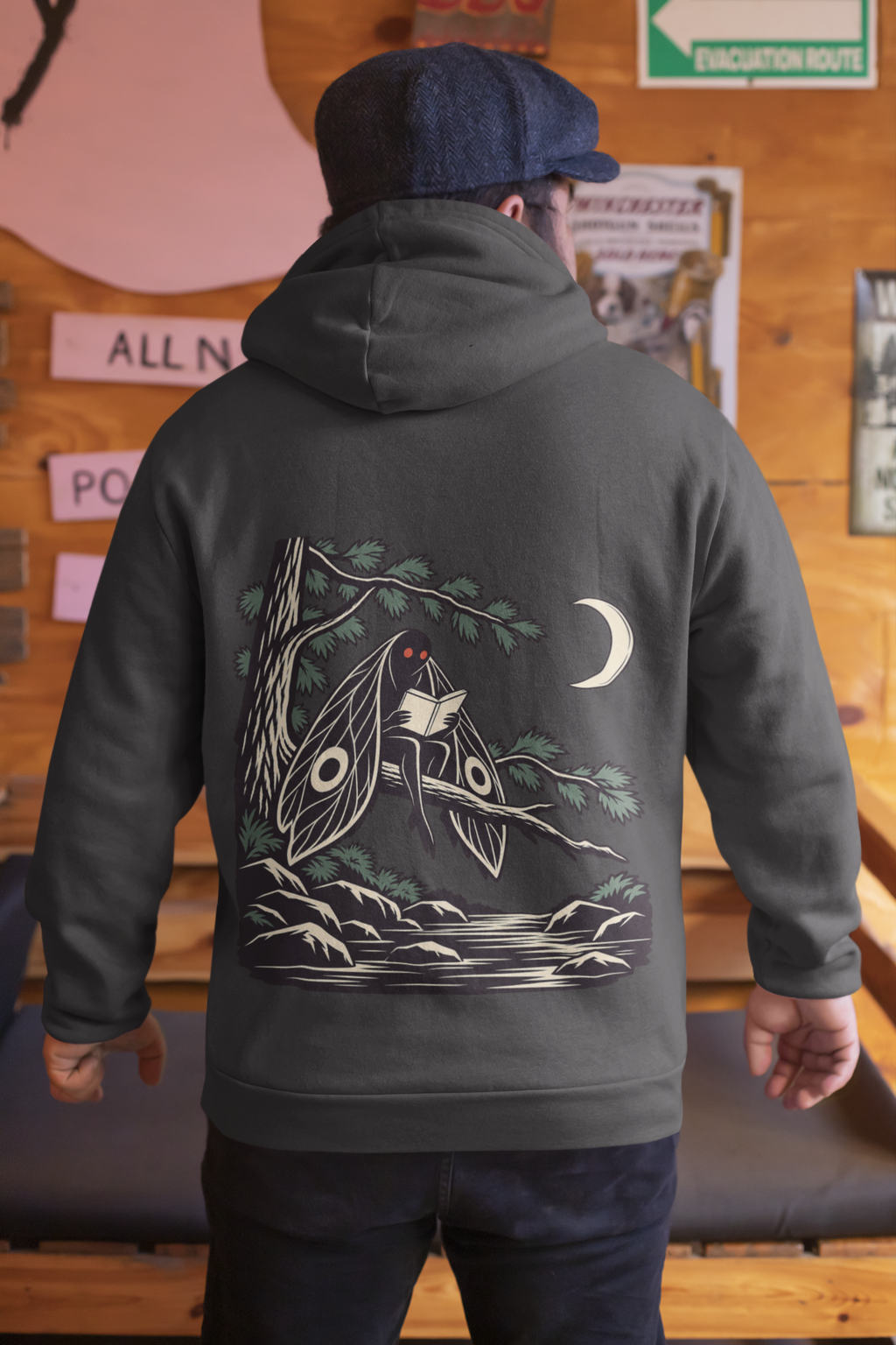 Night Library Heavyweight Hoodie in Black, worn by a man seen from behind in a wood-panelled bar, showing the large print on the back. Digital product mockup.