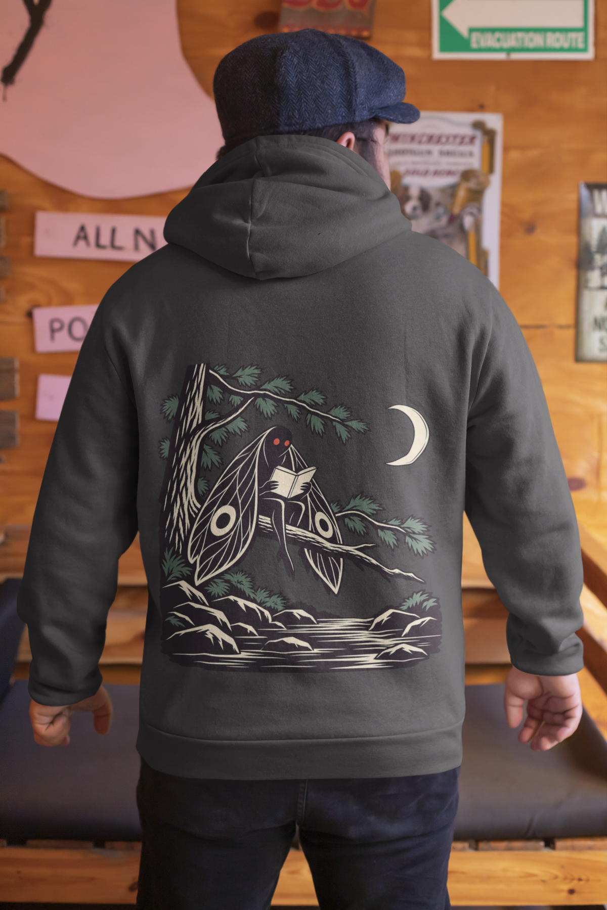 Night Library Heavyweight Hoodie in Black, worn by a man seen from behind in a wood-panelled bar, showing the large print on the back. Digital product mockup.