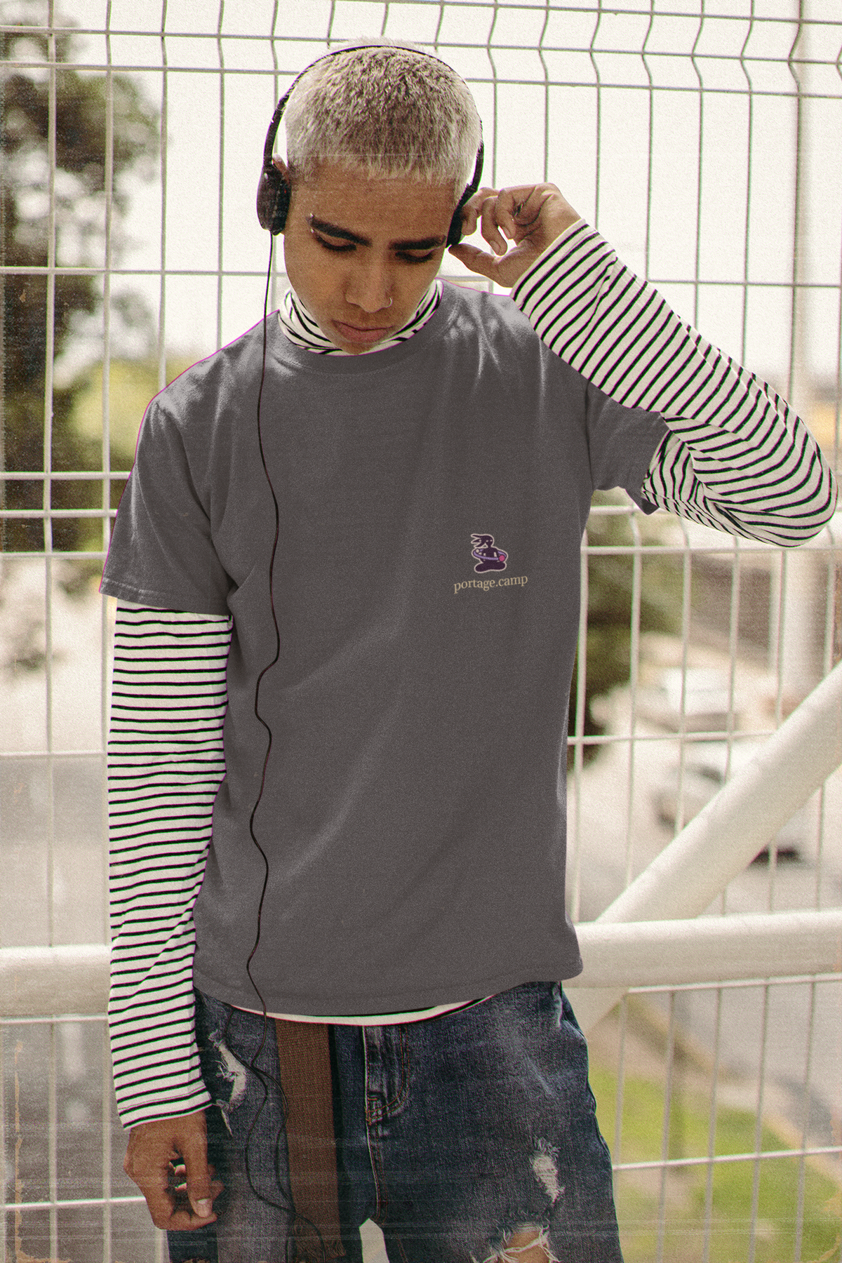 Orbit Keeper Garment-Dyed Tee in Navy, worn by a man in headphones by a fence, with the Orbit Keeper logo and portage.camp on the chest. Digital product mockup.