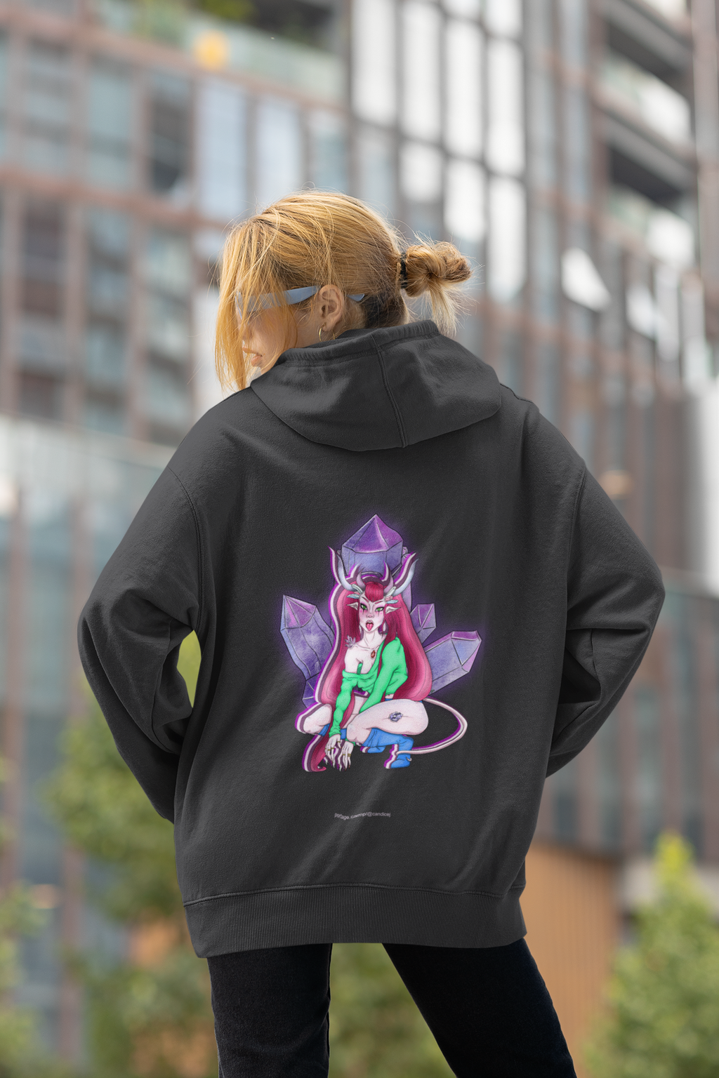 Heart Thief Heavyweight Hoodie in Black, worn by a woman seen from behind by tall city buildings, showing the large print on the back. Digital product mockup.