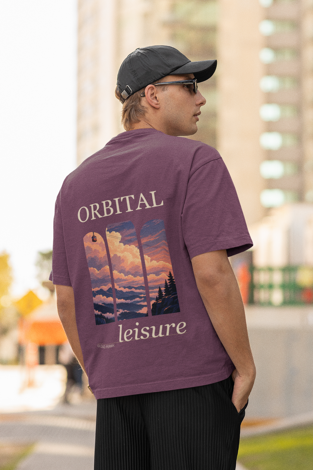 Cloud Ferry Garment-Dyed Tee in Berry, worn by a man seen from behind in a cap and sunglasses on a city street, showing the large print on the back. Digital product mockup.
