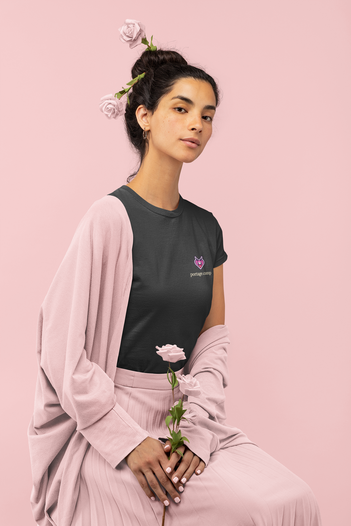Heart Thief Women’s Relaxed Tee in Black, worn by a woman holding a rose, with the Heart Thief logo and portage.camp on the chest. Digital product mockup.