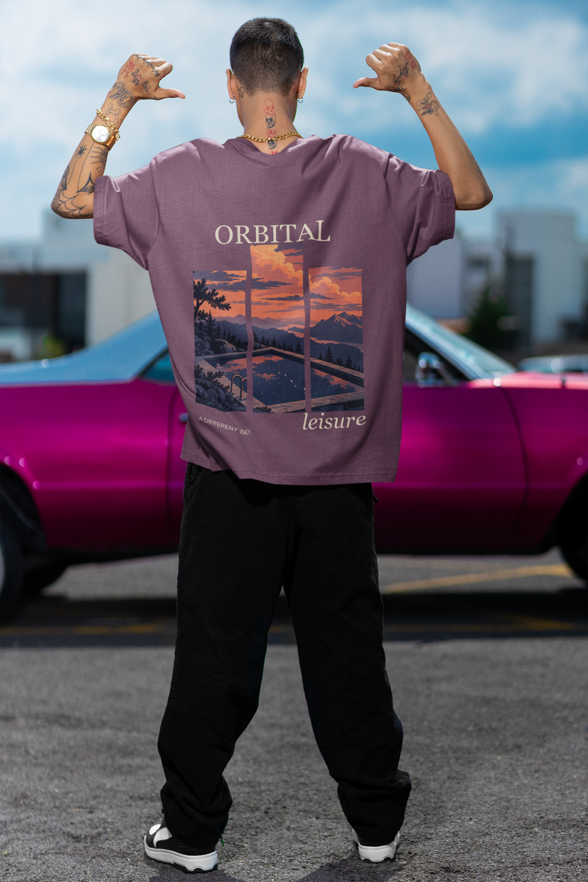 Amethyst After Hours Garment-Dyed Tee in Berry, worn by a man seen from behind by a pink car, showing the large print on the back. Digital product mockup.