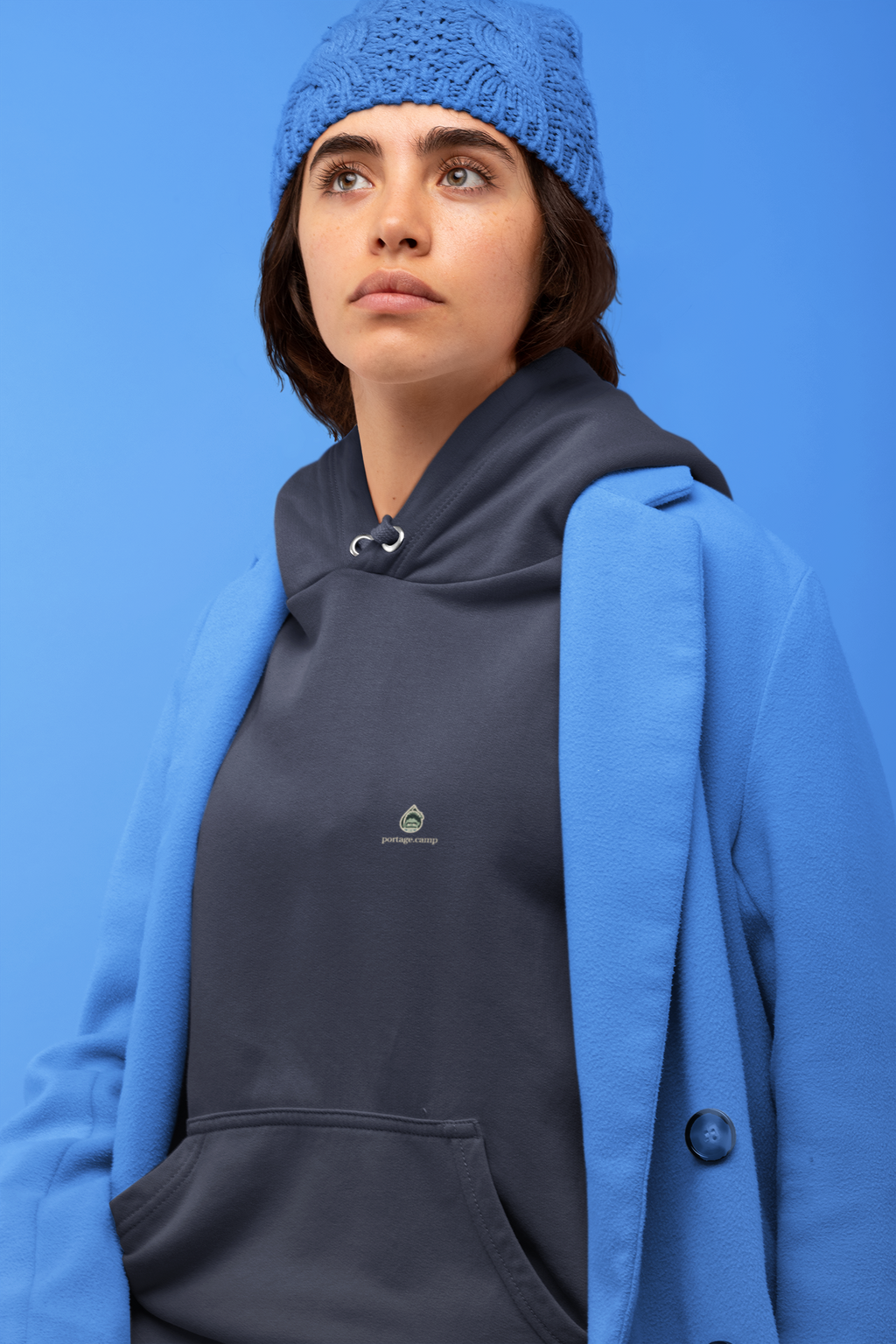 Rain Check Midweight Hoodie in Classic Navy, worn by a woman against a blue backdrop, with the Rain Check logo and portage.camp on the chest. Digital product mockup.
