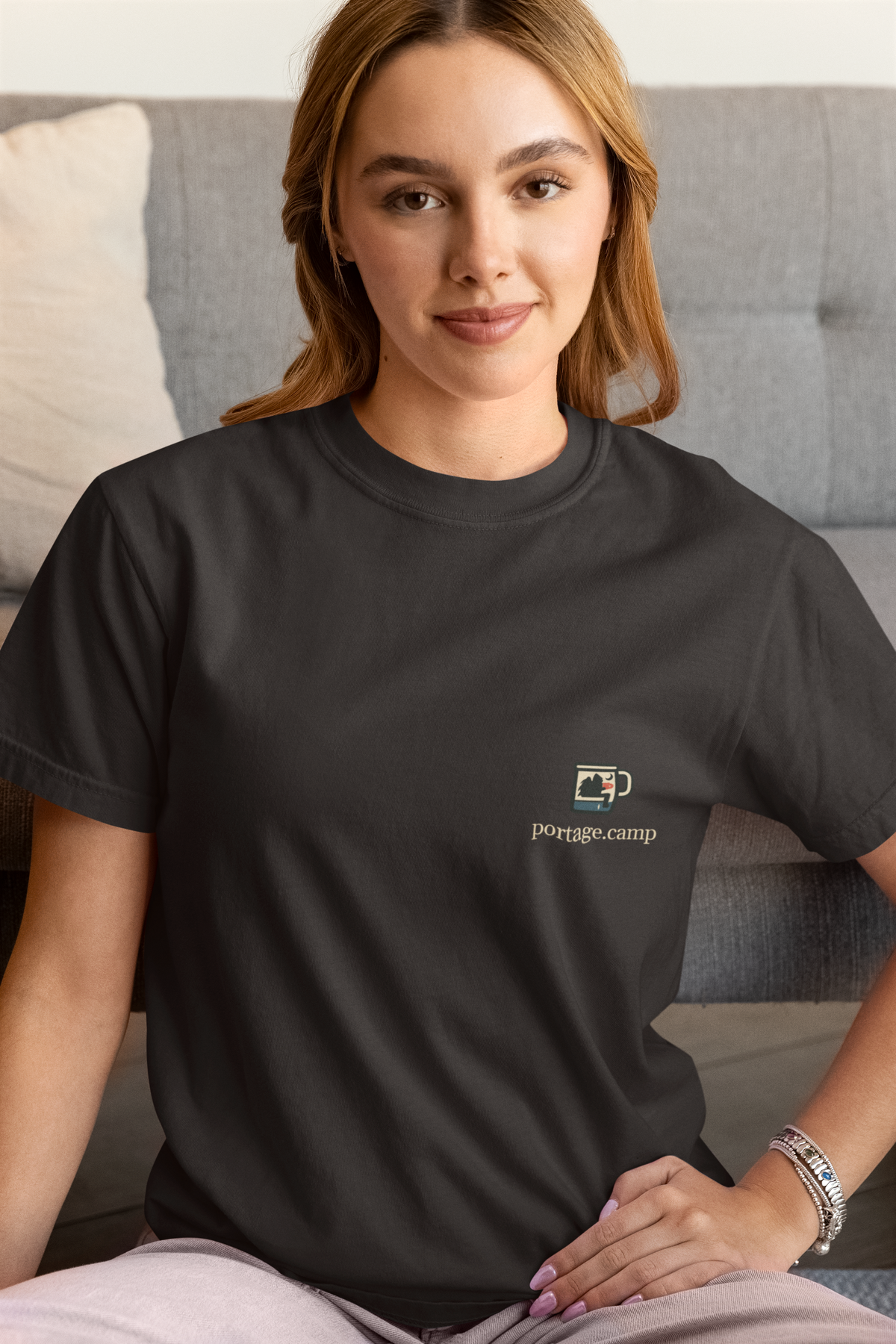 Quiet Hours Garment-Dyed Tee in Black, worn by a woman at home, with the Quiet Hours logo and portage.camp on the chest. Digital product mockup.