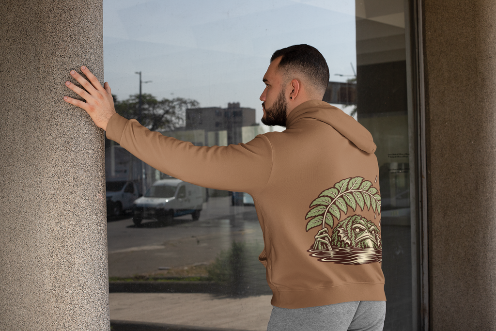 Rain Check Midweight Hoodie in Saddle, worn by a man seen from behind leaning on a pillar by a window, showing the large print on the back. Digital product mockup.