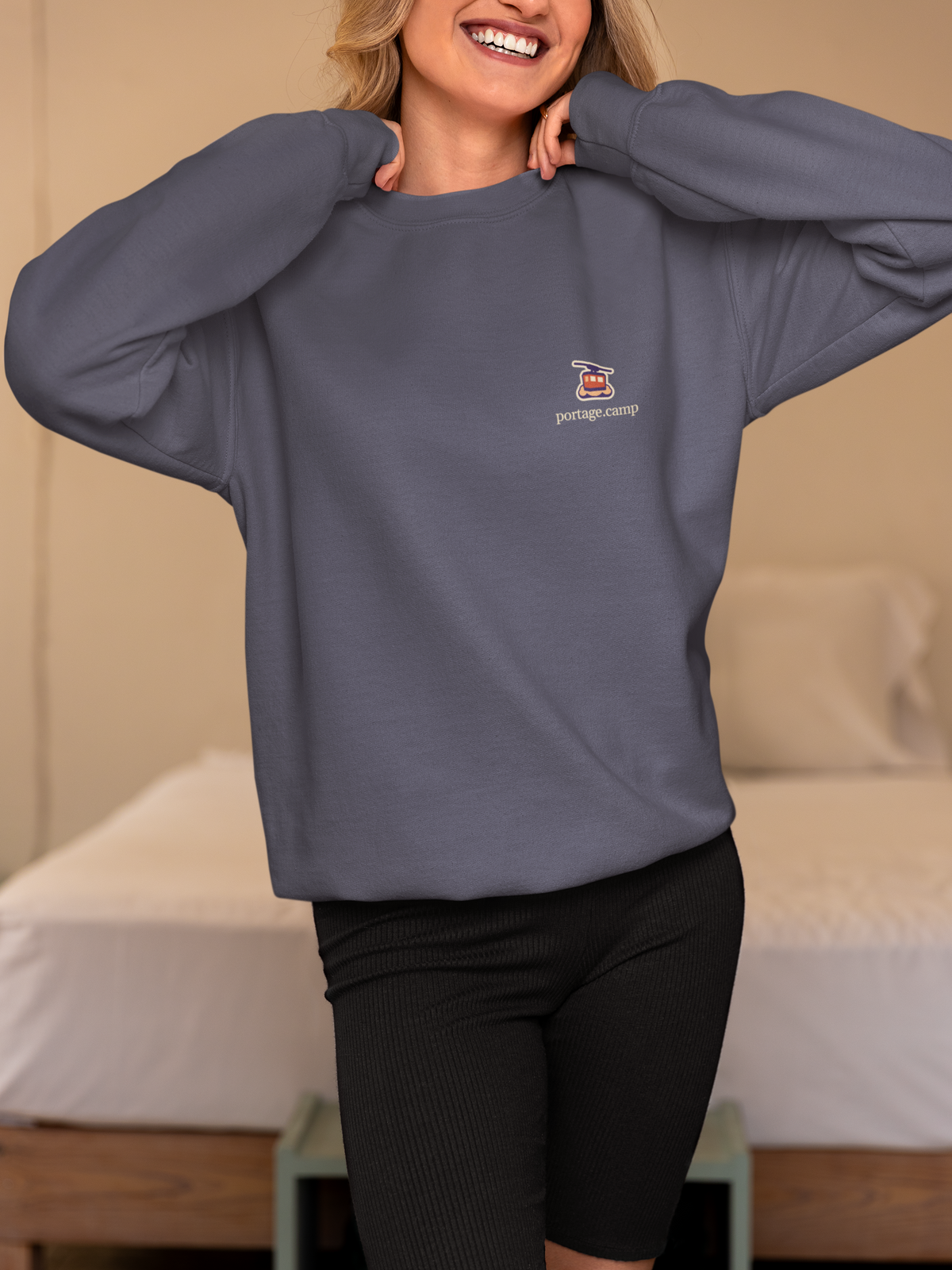 Cloud Ferry Garment-Dyed Crewneck in Denim, worn by a woman in a bedroom, with the Cloud Ferry logo and portage.camp on the chest. Digital product mockup.