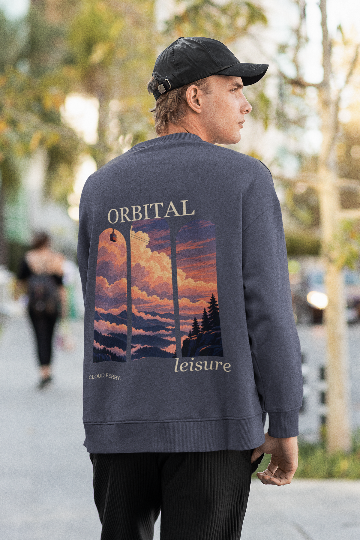 Cloud Ferry Garment-Dyed Crewneck in Denim, worn by a man seen from behind walking down a city street, showing the large print on the back. Digital product mockup.