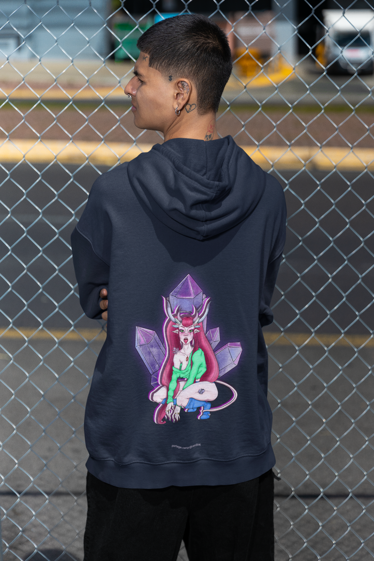 Amethyst After Hours Zip Hoodie in Navy, worn by a man seen from behind by a chain-link fence, showing the large print on the back. Digital product mockup.