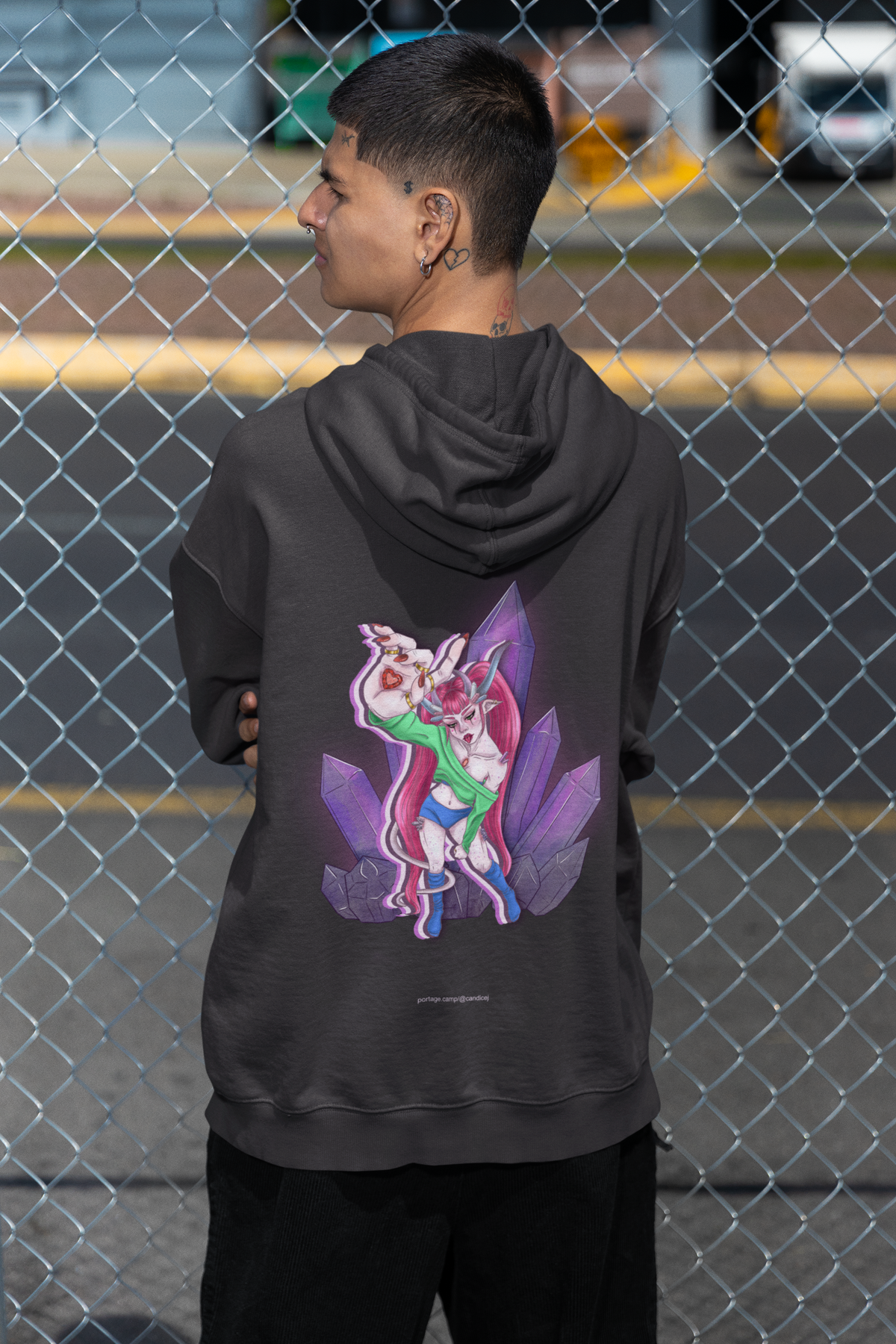 Amethyst After Hours Midweight Hoodie in Black, worn by a man seen from behind by a chain-link fence, showing the large print on the back. Digital product mockup.