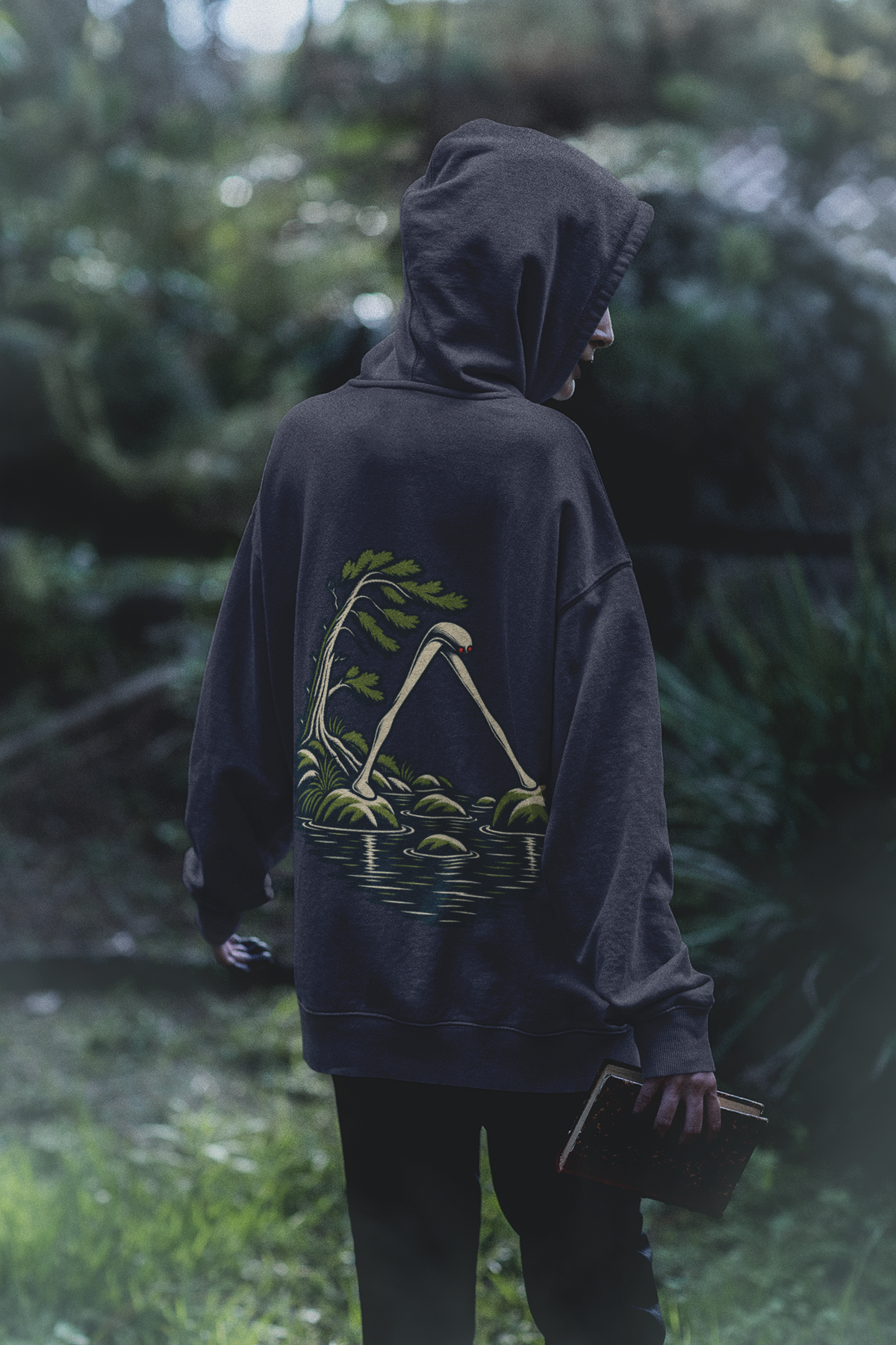 Small Hours Midweight Hoodie in Classic Navy, worn by a woman seen from behind in a dark forest, showing the large print on the back. Digital product mockup.
