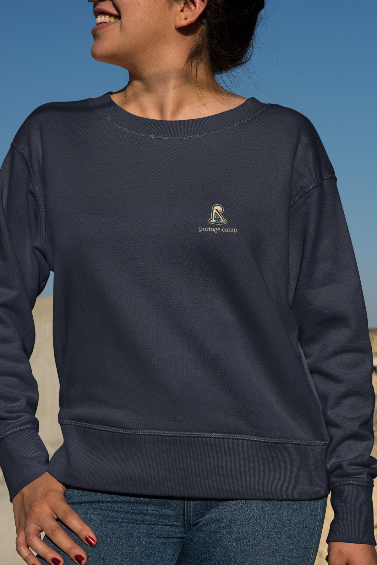 Small Hours Garment-Dyed Crewneck in True Navy, worn by a woman against a plain backdrop, with the Small Hours logo and portage.camp on the chest. Digital product mockup.