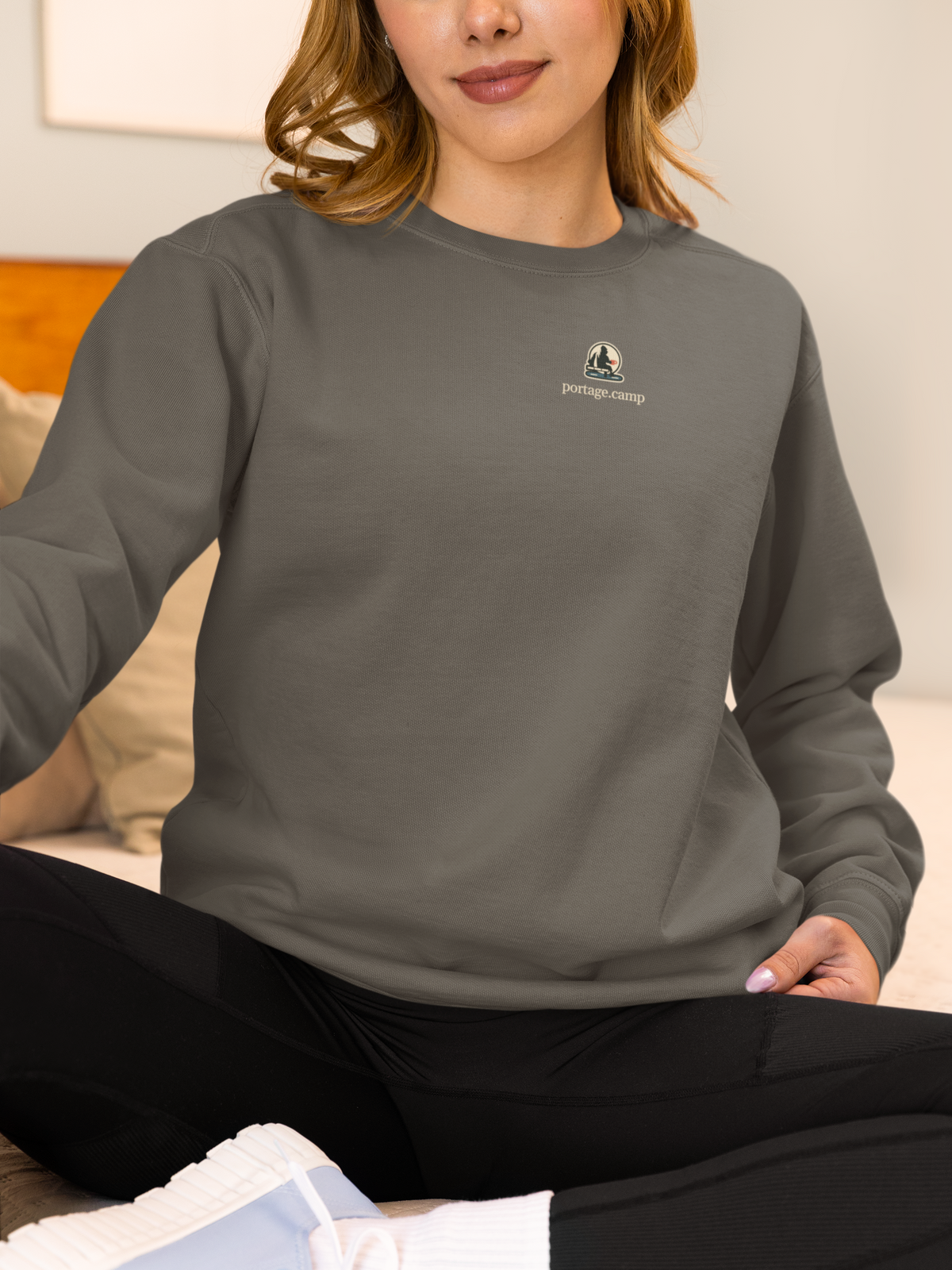 Quiet Hours Garment-Dyed Crewneck in Pepper, worn by a woman at home, with the Quiet Hours logo and portage.camp on the chest. Digital product mockup.