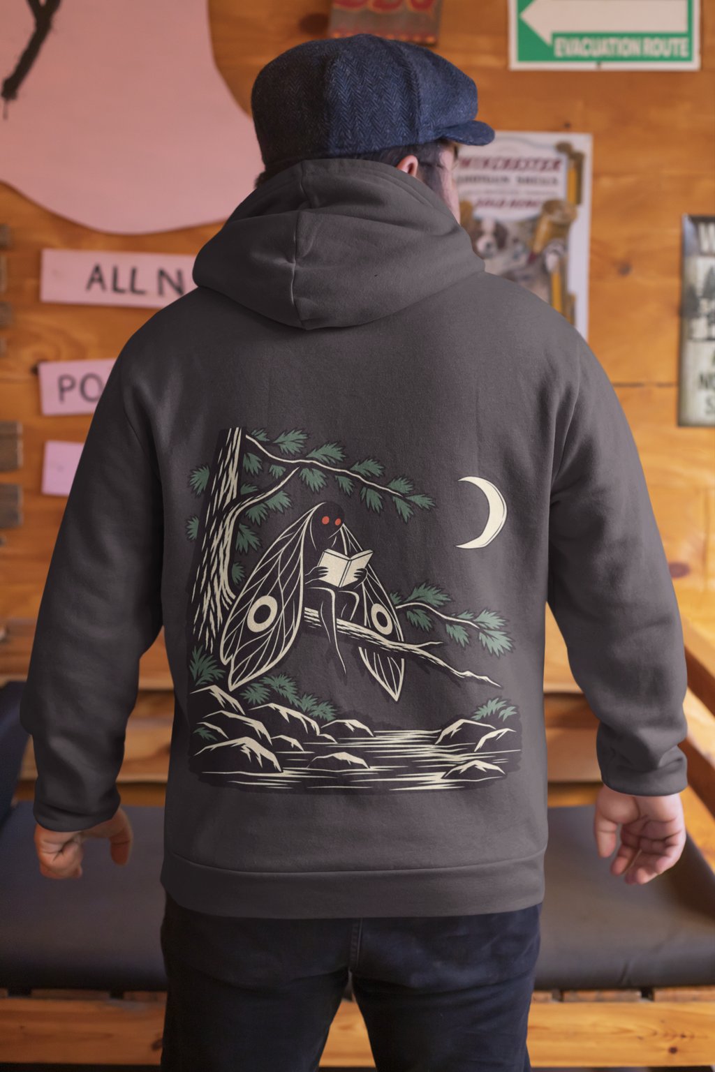 Night Library Midweight Hoodie in Black, worn by a man seen from behind in a wood-panelled bar, showing the large print on the back. Digital product mockup.