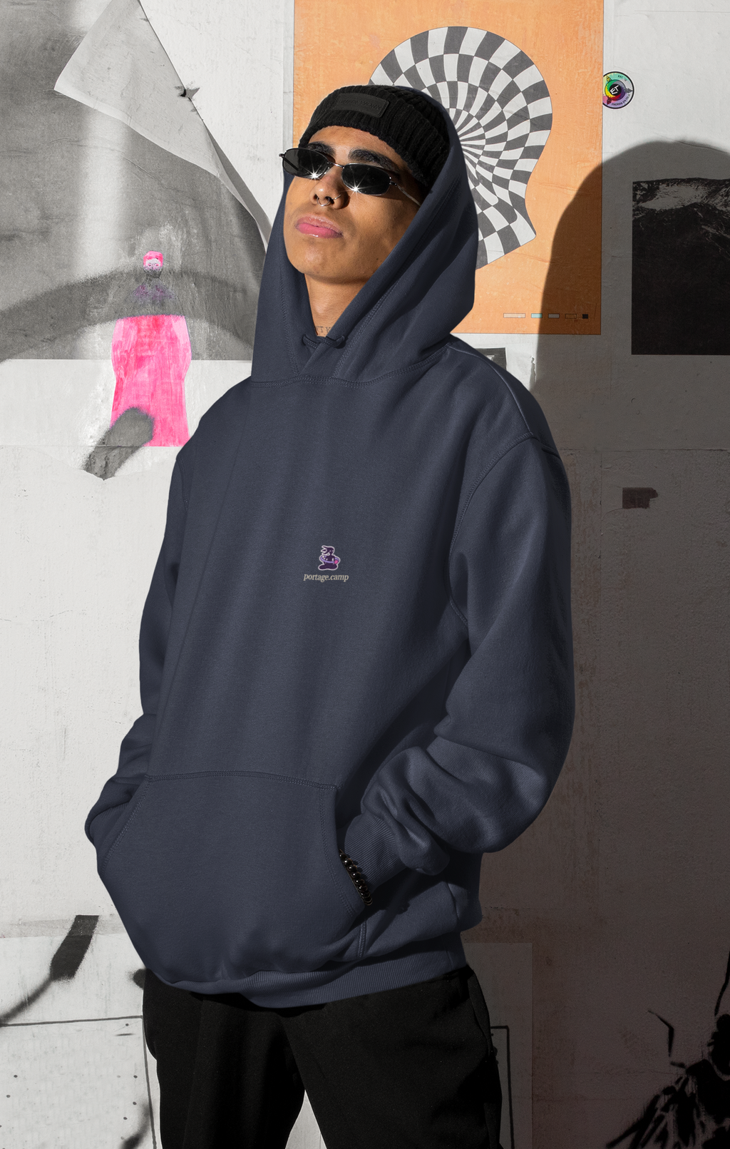 Orbit Keeper Midweight Hoodie in Classic Navy, worn by a man by a wall of posters, with the Orbit Keeper logo and portage.camp on the chest. Digital product mockup.