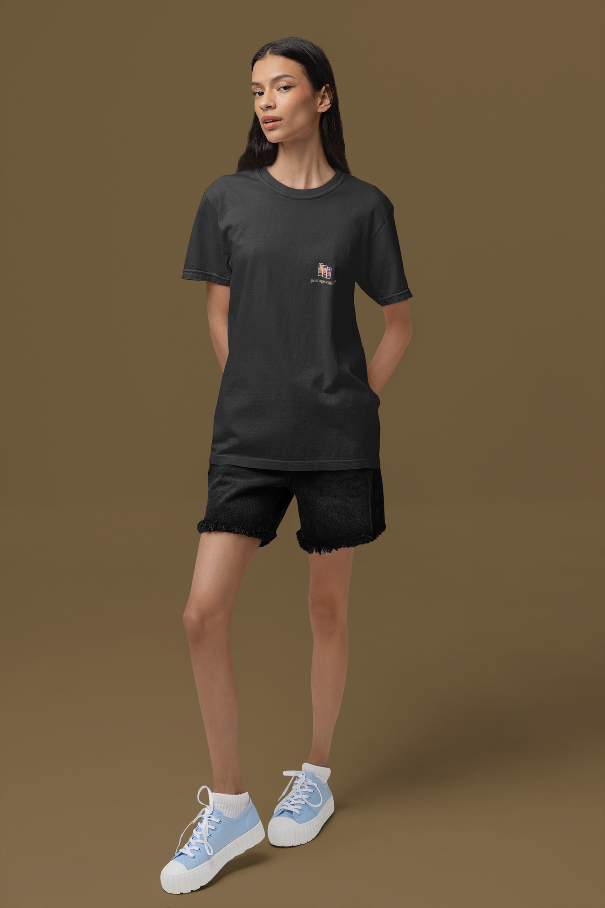 Stay for the Sky Garment-Dyed Tee in Black, worn by a woman standing in a studio, with the Stay for the Sky logo and portage.camp on the chest. Digital product mockup.