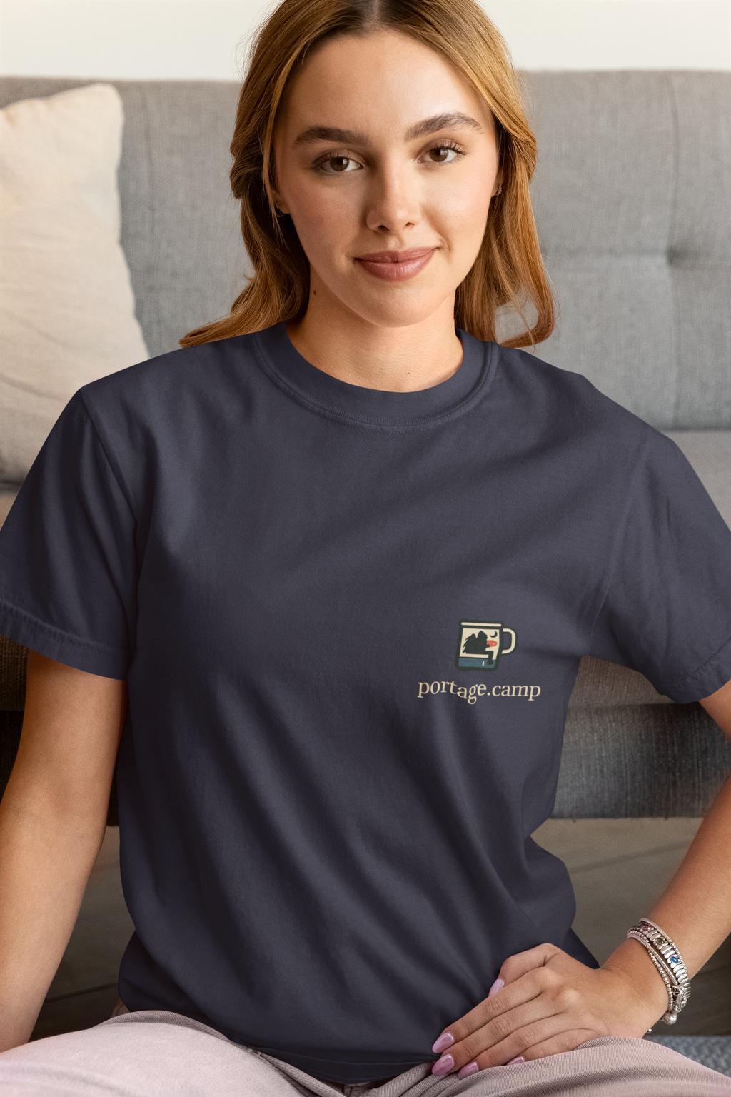 Quiet Hours Women’s Relaxed Tee in Navy, worn by a woman at home, with the Quiet Hours logo and portage.camp on the chest. Digital product mockup.