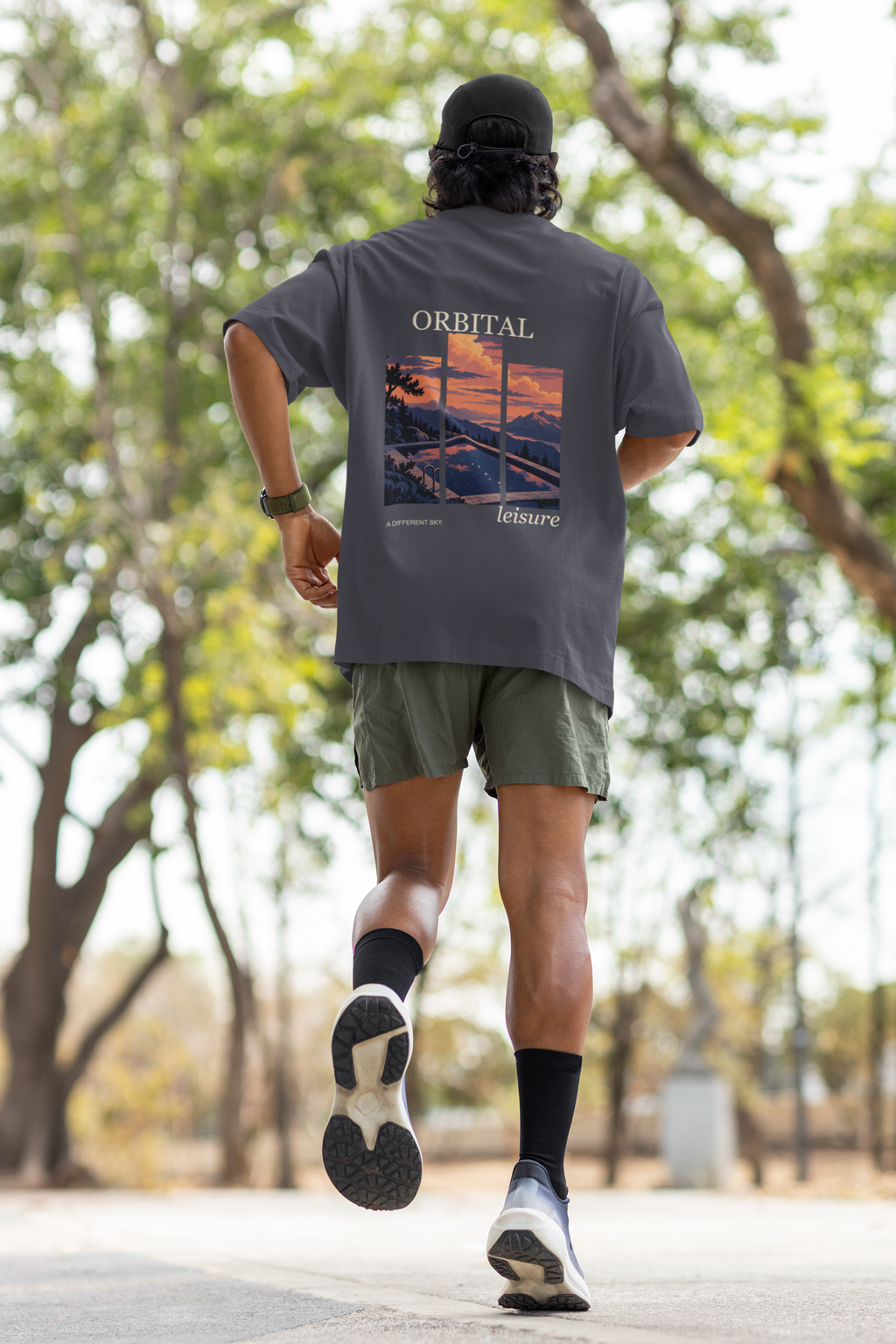 A Different Sky Garment-Dyed Tee in Navy, worn by a man seen from behind jogging through a park, showing the large print on the back. Digital product mockup.