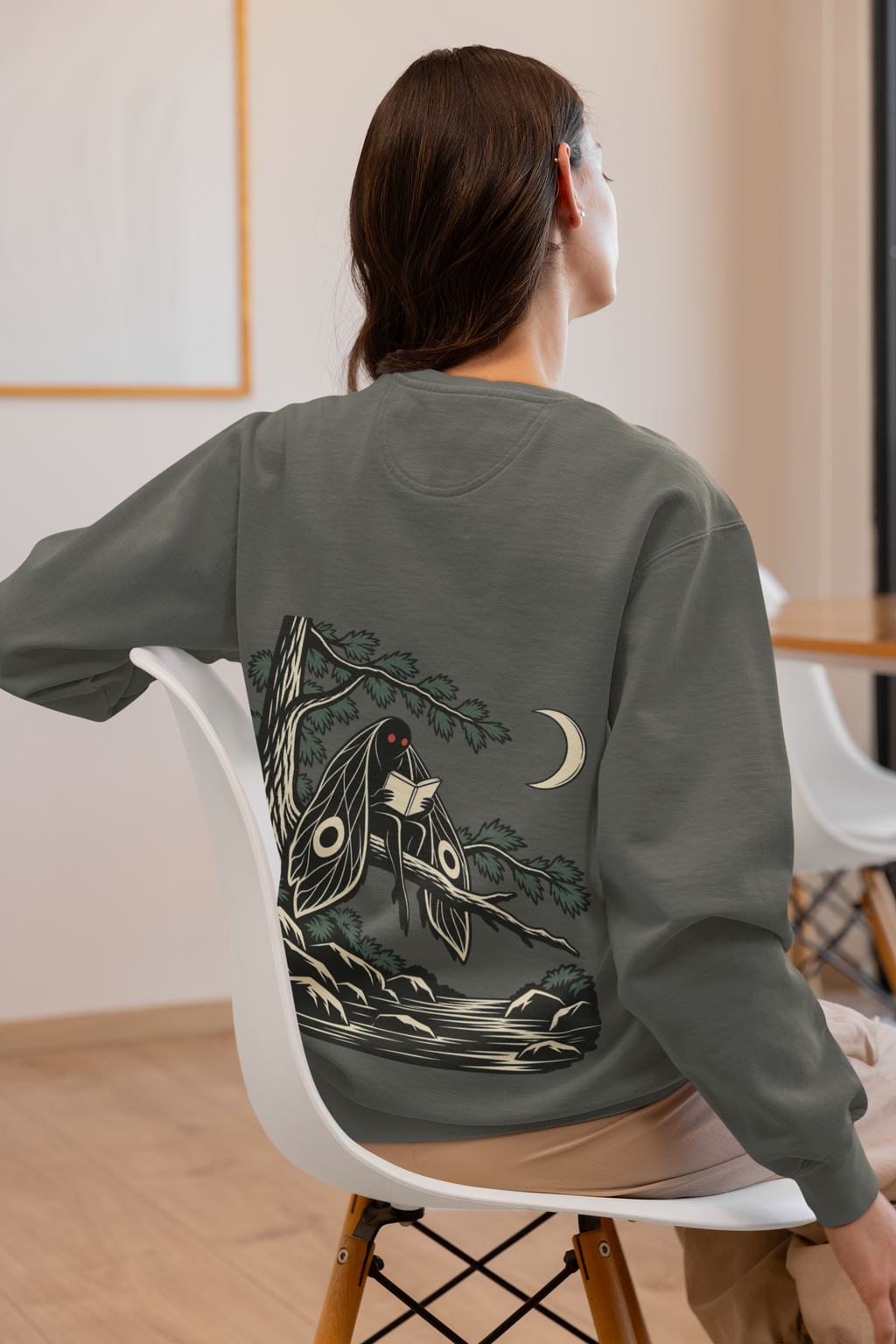 Night Library Garment-Dyed Crewneck in Pepper, worn by a woman seen from behind at home, showing the large print on the back. Digital product mockup.