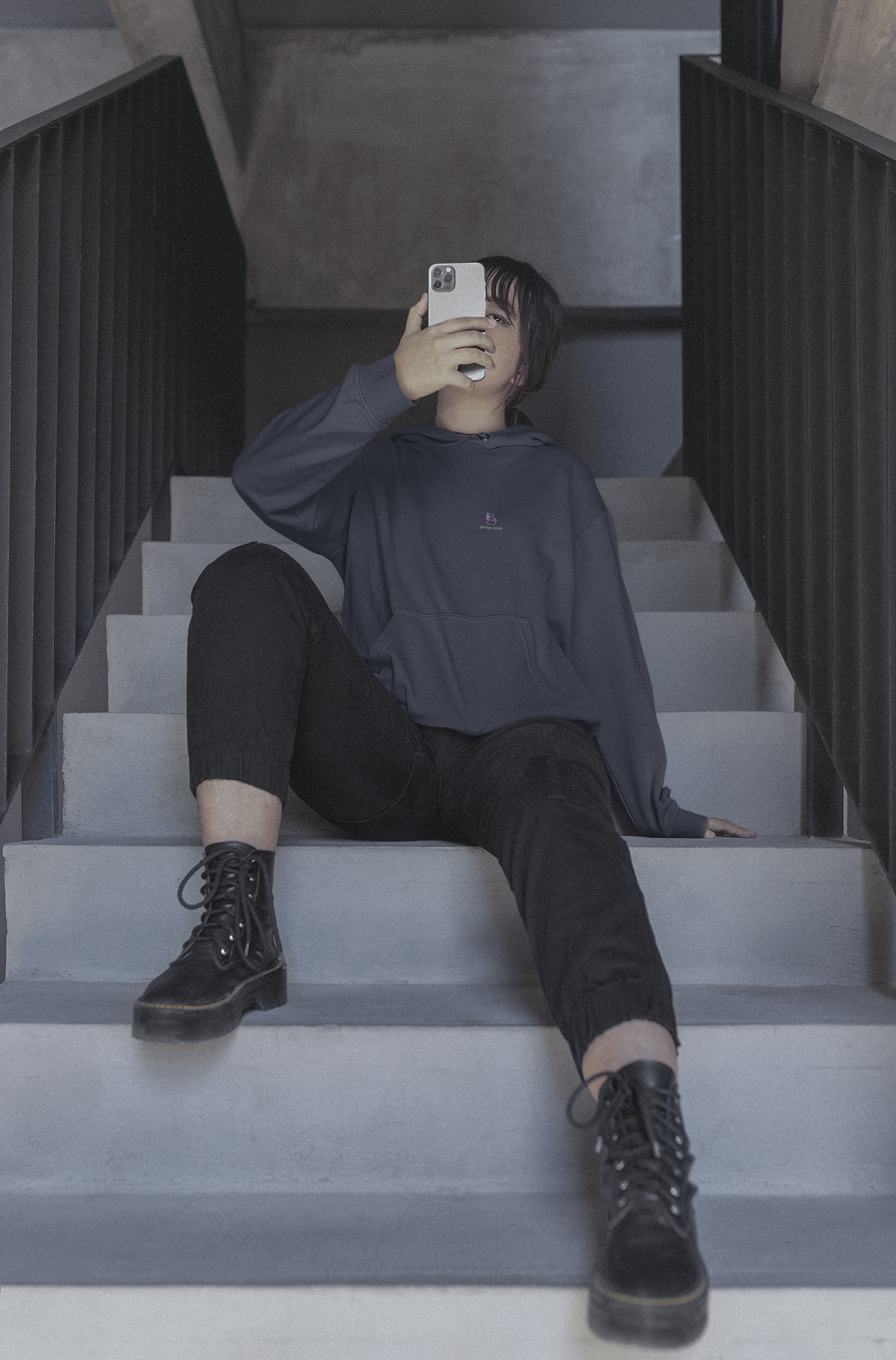Orbit Keeper Midweight Hoodie in Classic Navy, worn by a woman seated on a staircase, with the Orbit Keeper logo and portage.camp on the chest. Digital product mockup.