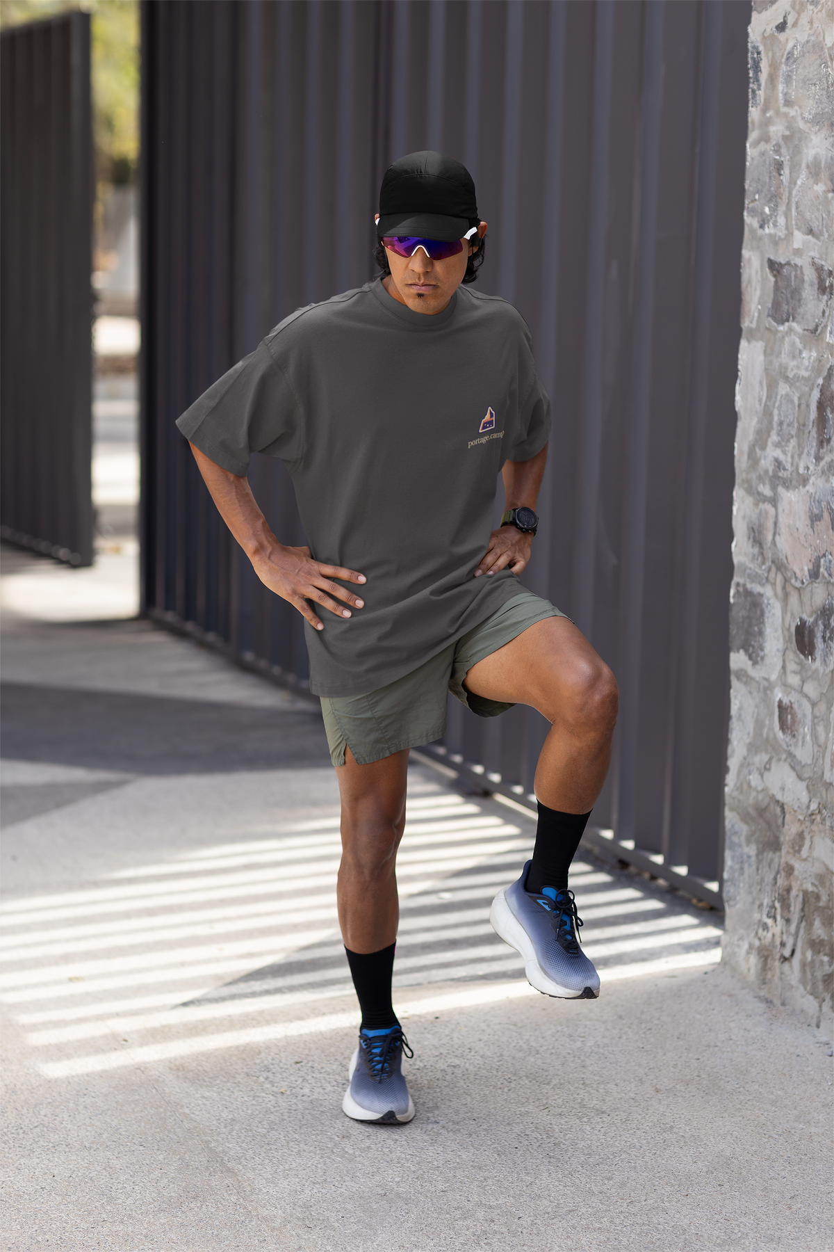A Different Sky Garment-Dyed Tee in Graphite, worn by a man stretching before a run, with the A Different Sky logo and portage.camp on the chest. Digital product mockup.