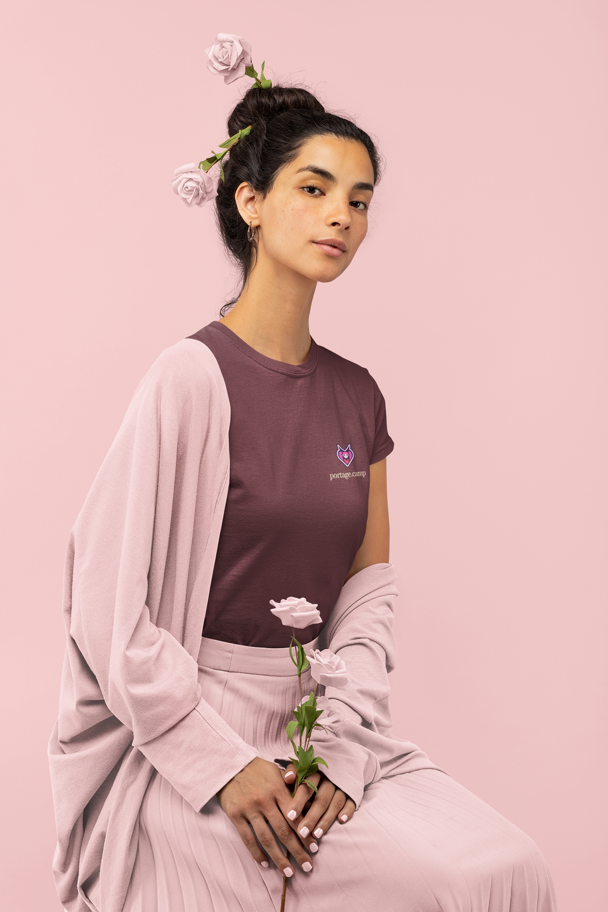 Heart Thief Women’s Relaxed Tee in Maroon, worn by a woman holding a rose, with the Heart Thief logo and portage.camp on the chest. Digital product mockup.