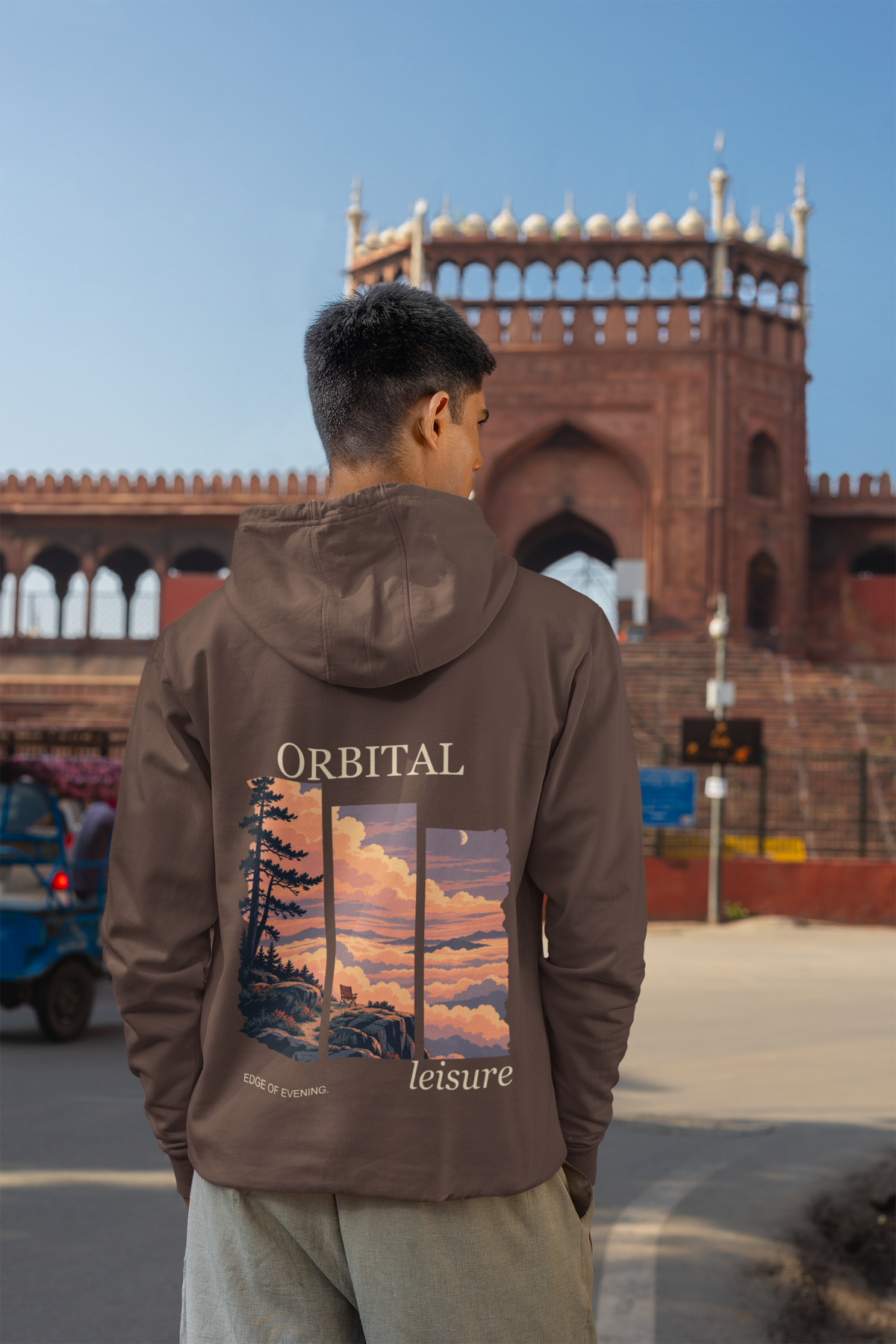 A Different Sky Heavyweight Hoodie in Brown, worn by a man seen from behind on a city street, showing the large print on the back. Digital product mockup.