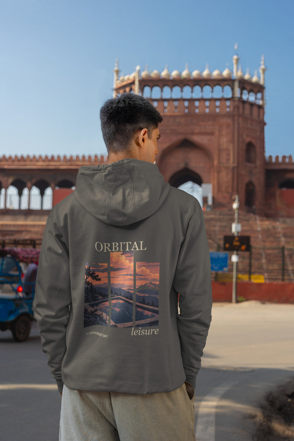 A Different Sky Zip Hoodie in Dark Heather, worn by a man seen from behind on a city street, showing the large print on the back. Digital product mockup.