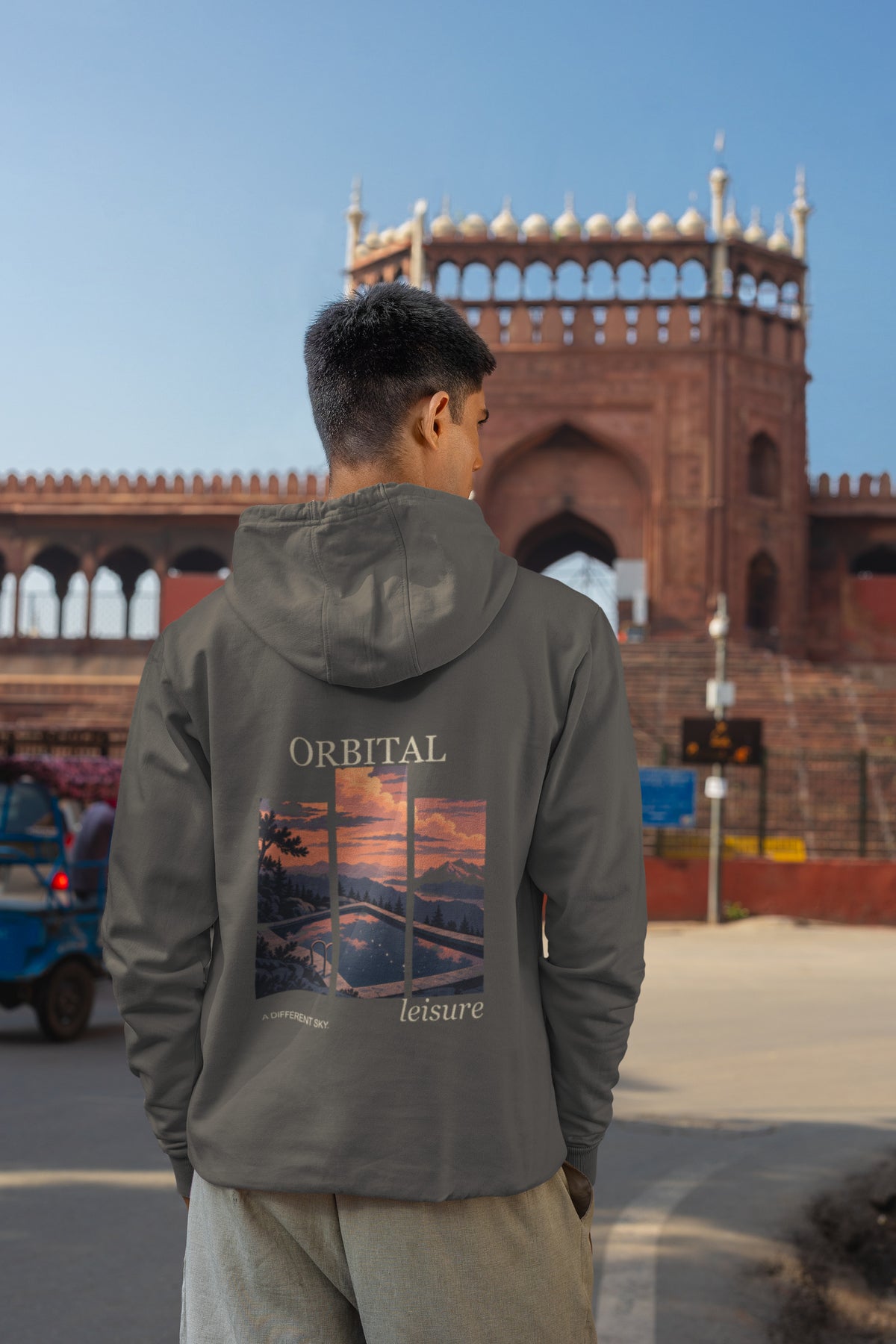 A Different Sky Zip Hoodie in Dark Heather, worn by a man seen from behind on a city street, showing the large print on the back. Digital product mockup.