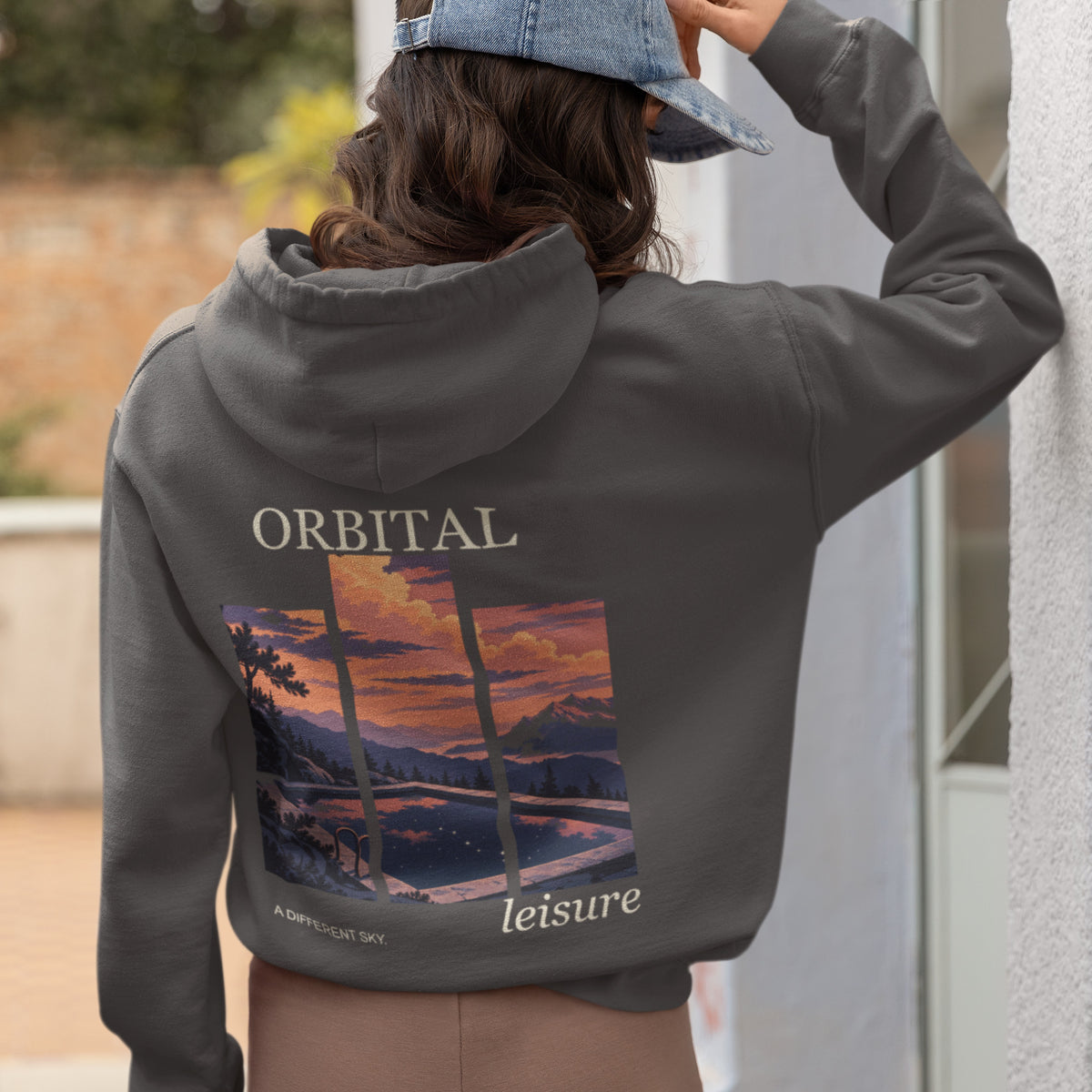 A Different Sky Zip Hoodie in Dark Heather, worn by a woman seen from behind at home, showing the large print on the back. Digital product mockup.