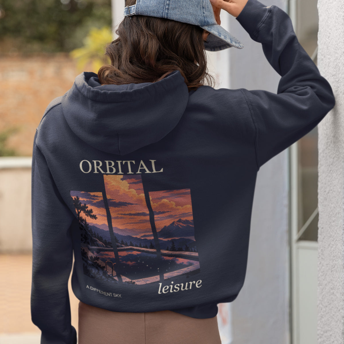 A Different Sky Zip Hoodie in Navy, worn by a woman seen from behind at home, showing the large print on the back. Digital product mockup.