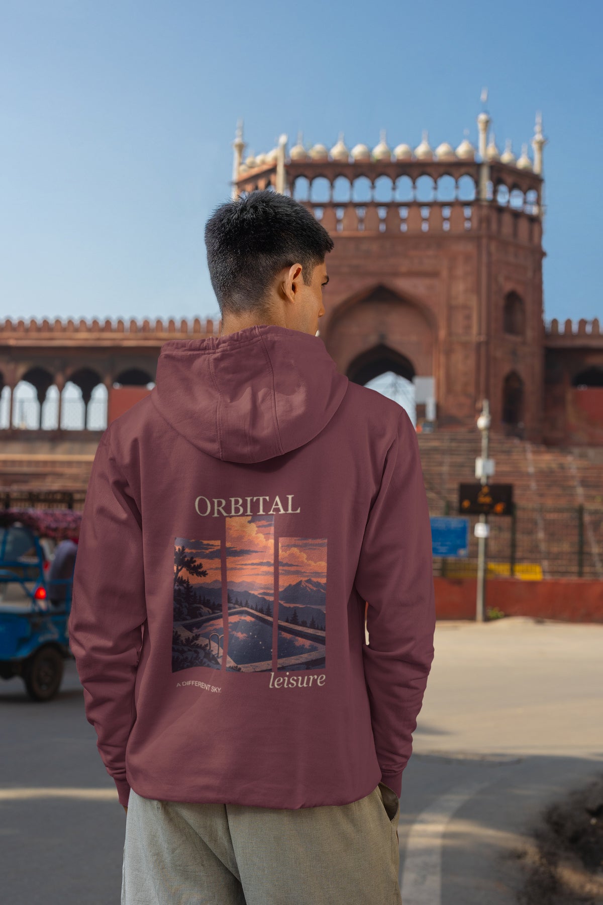 A Different Sky Zip Hoodie in Maroon, worn by a man seen from behind on a city street, showing the large print on the back. Digital product mockup.