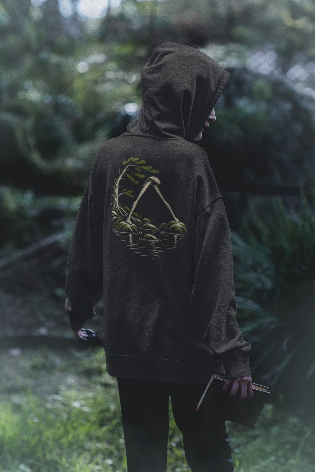 Small Hours Zip Hoodie in Black, worn by a woman seen from behind in a dark forest, showing the large print on the back. Digital product mockup.